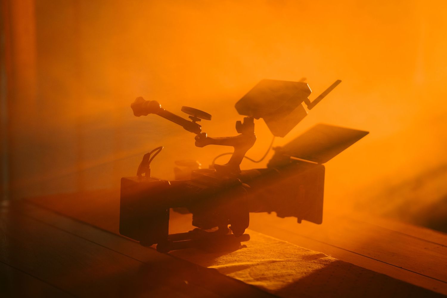 Silhouette of camera equipment against dramatic orange backlight creating atmospheric scene.