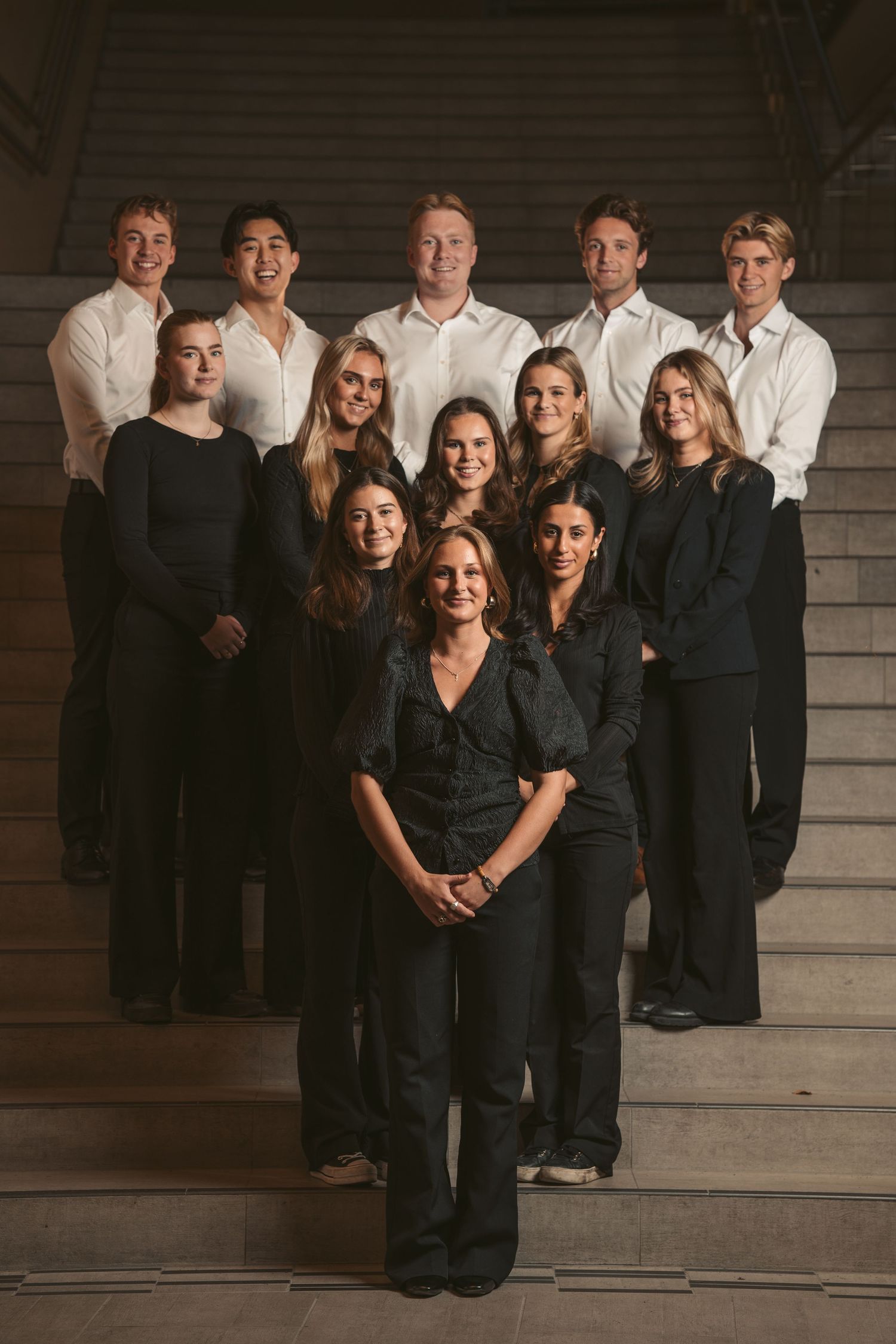 A formal group photo of people in black and white attire posed on stone steps.