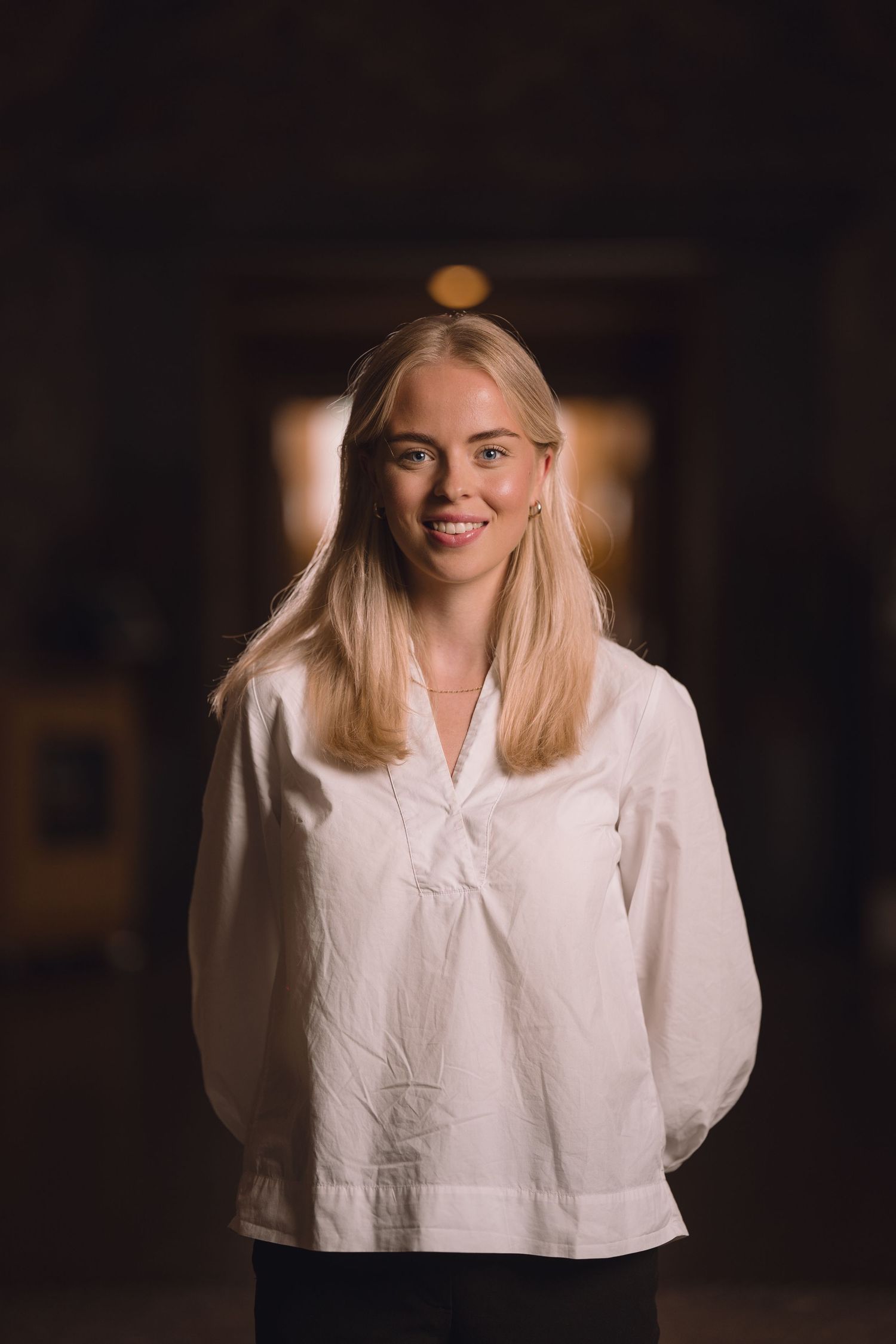 Woman in white blouse smiling warmly against dark background in artistic portrait series.