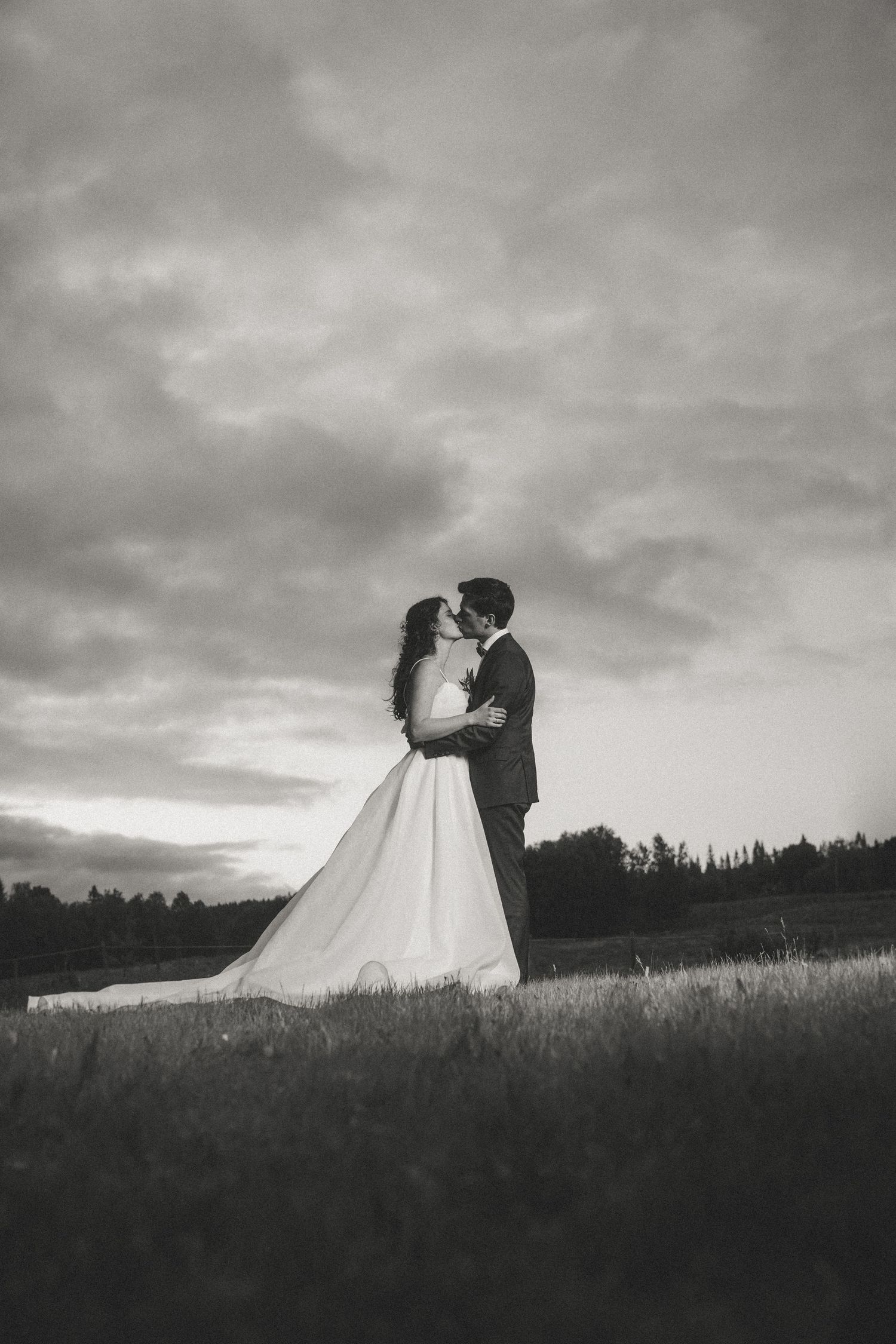 Dramatic black and white silhouettes of a wedding couple against a cloudy sunset sky.