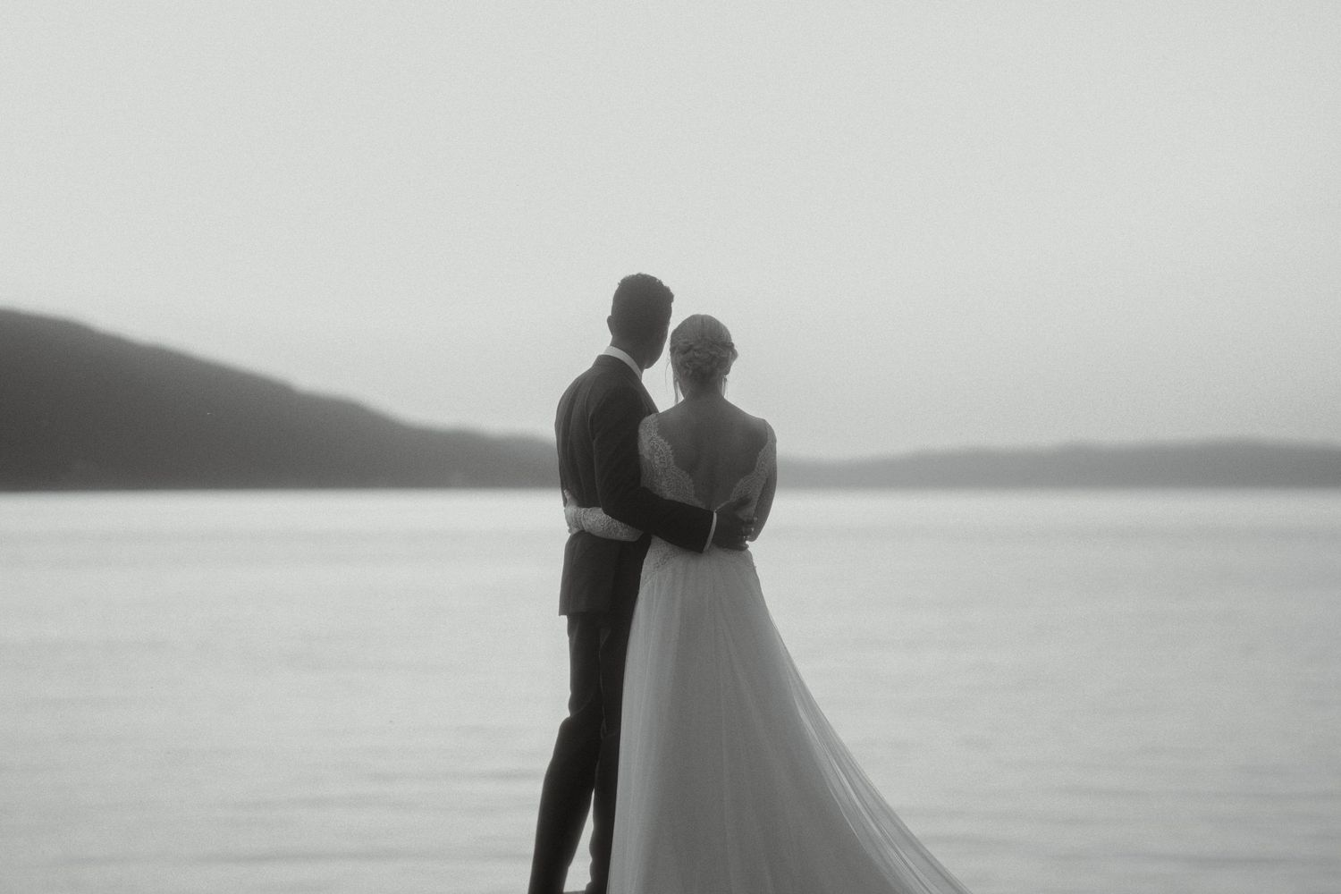 A minimalist black and white wedding photo of a couple silhouetted against a serene lake landscape.