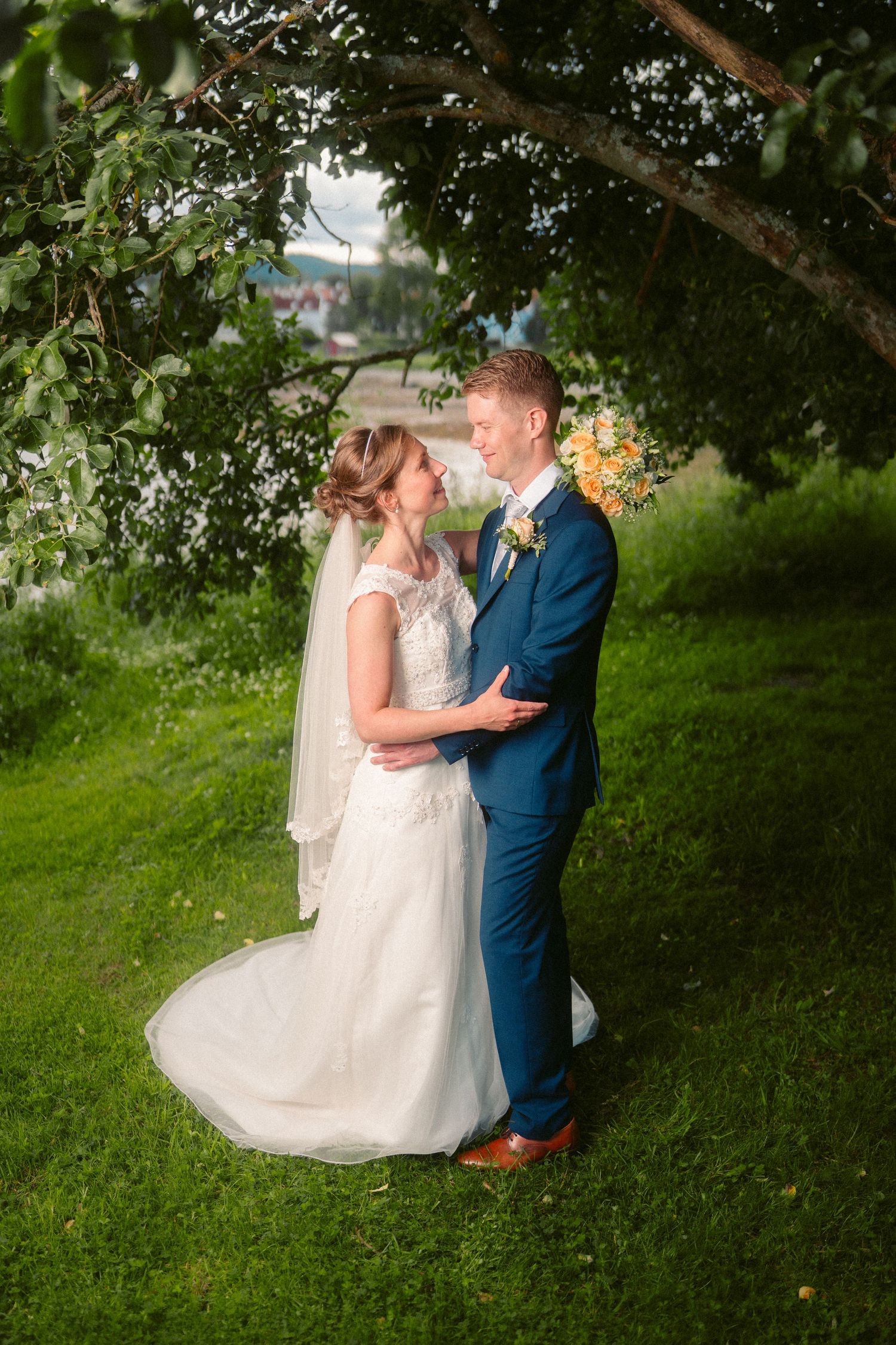 A wedding couple shares intimate moments under green trees in a garden setting.