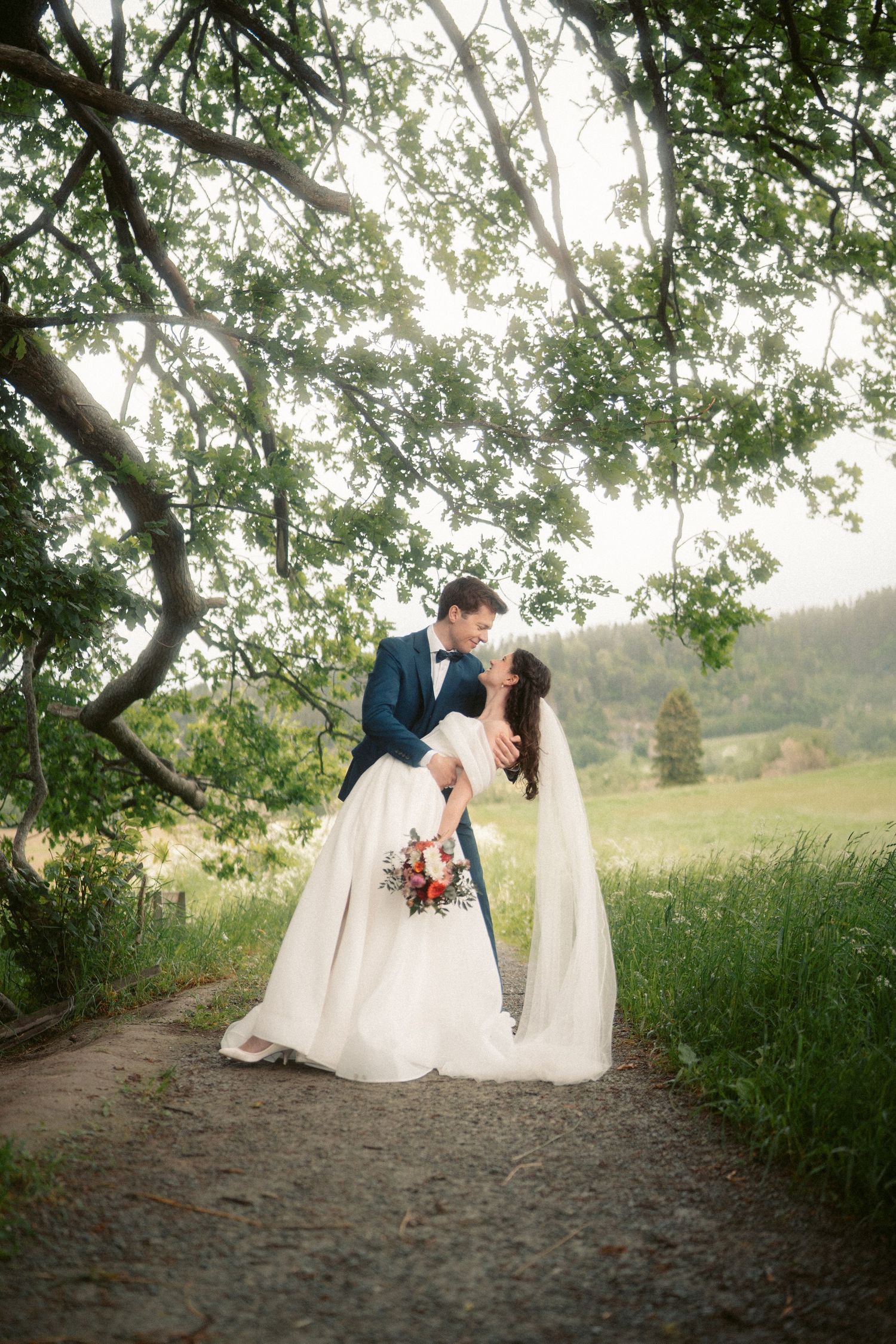 Wedding couple shares tender moments on a tree-lined path in nature.