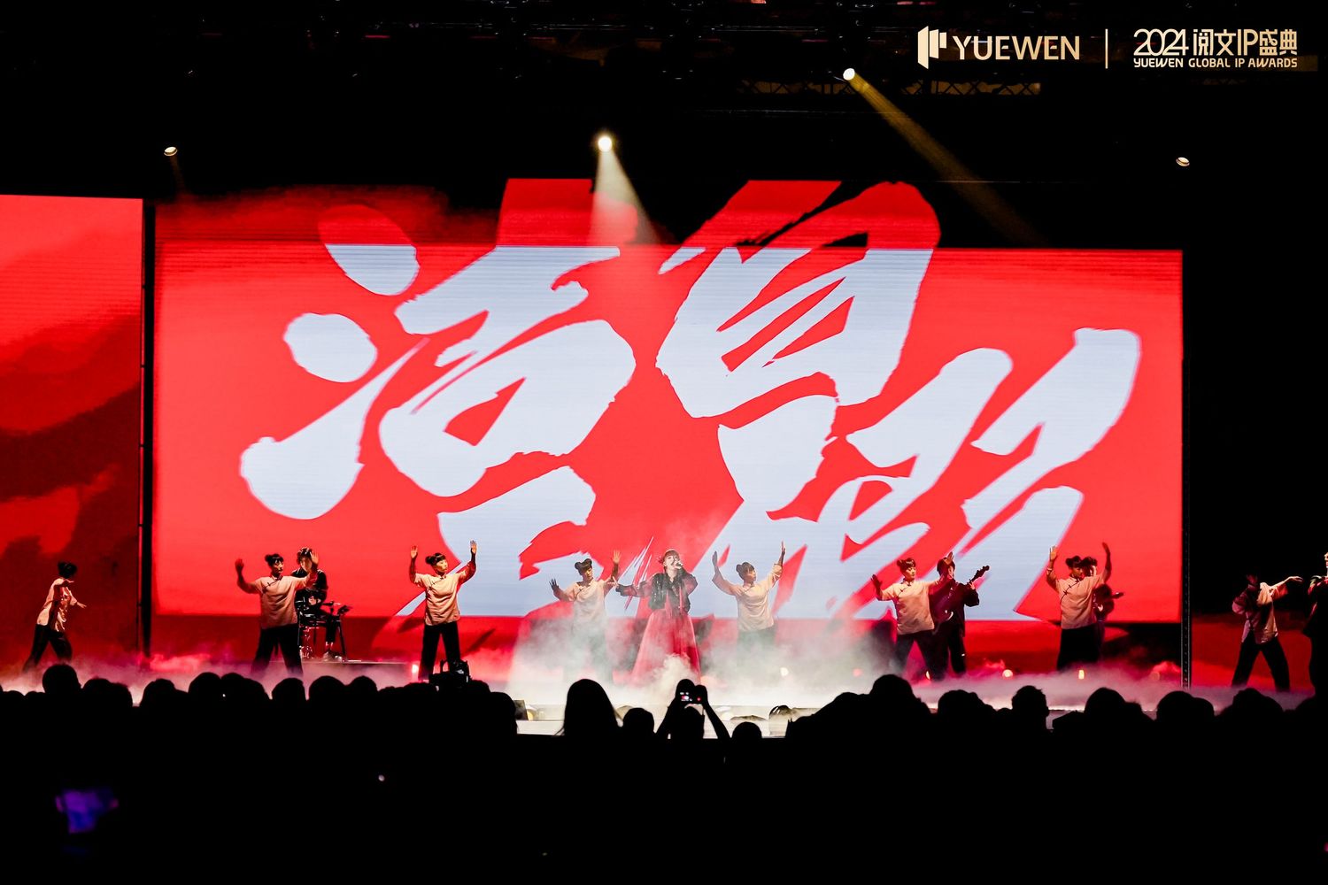 Performers dance on stage at a Yuewen cultural ceremony with bold red Chinese calligraphy backdrop and dramatic lighting.