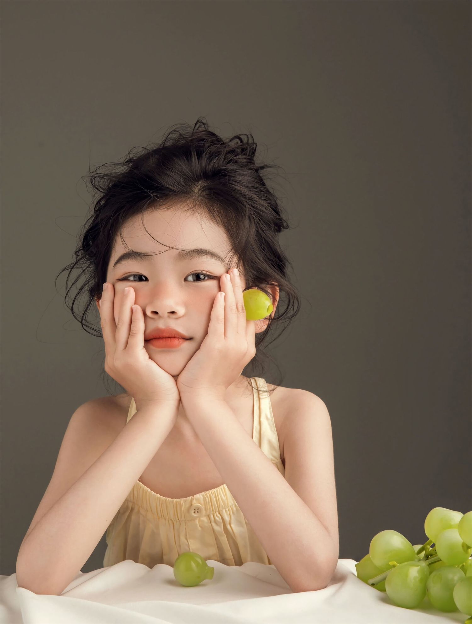 A series of artistic photos showing a child resting their head on their hands with green grapes on a table.