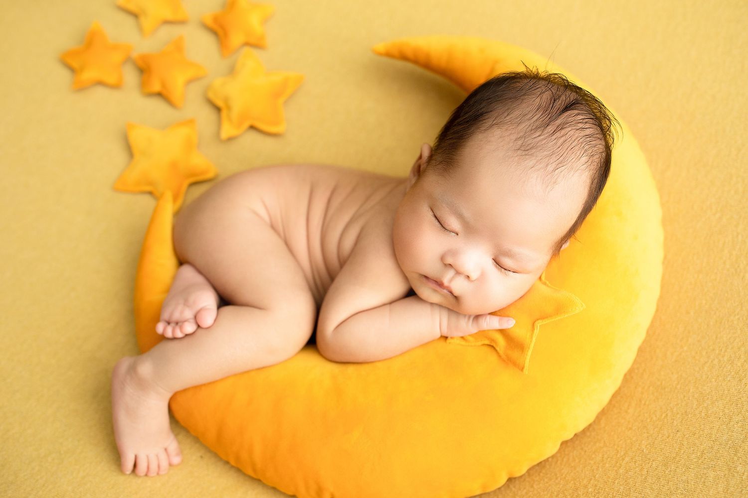 Sleeping baby in yellow swaddle blanket surrounded by star-shaped decorations on yellow background.