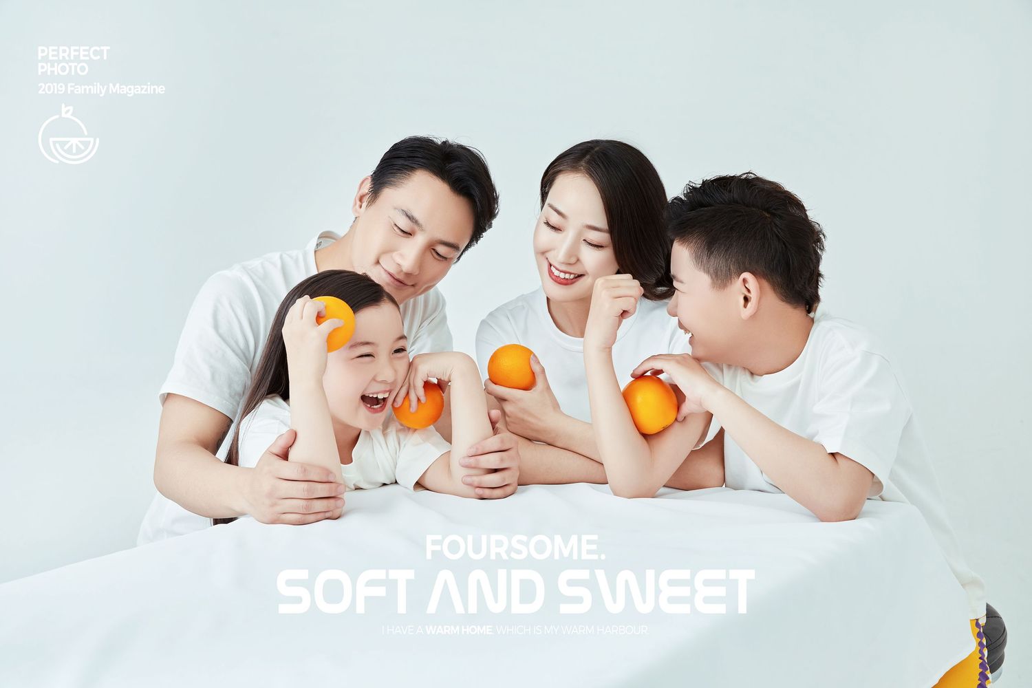 Three people in white shirts lay together on a white surface while holding fresh oranges.