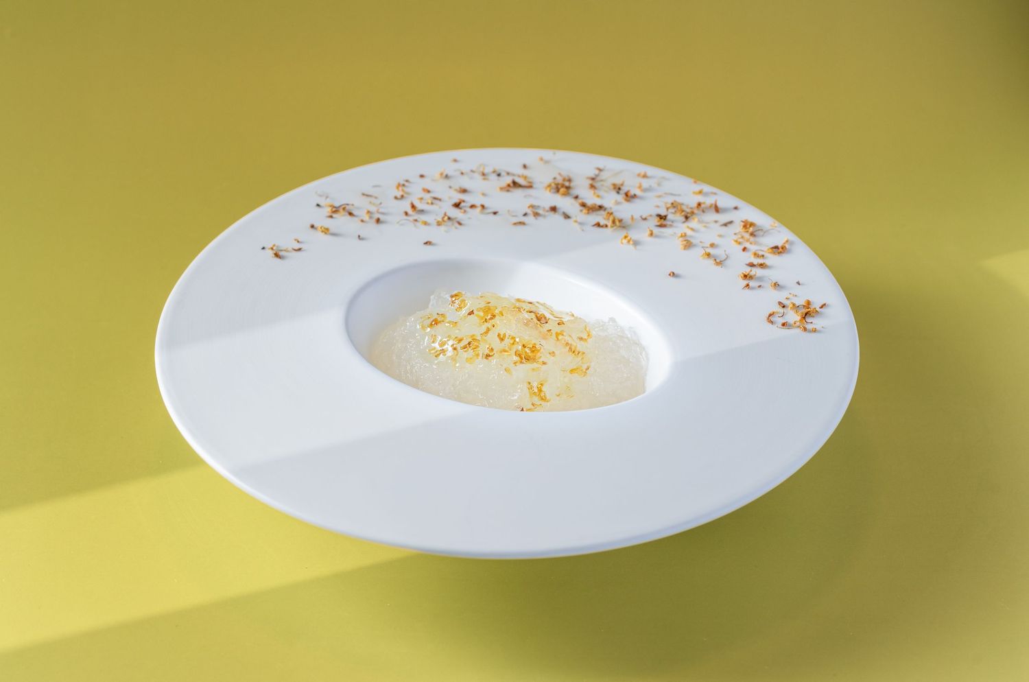 Elegant white wide-rimmed plate with creamy soup garnished with saffron and herbs on a yellow background.