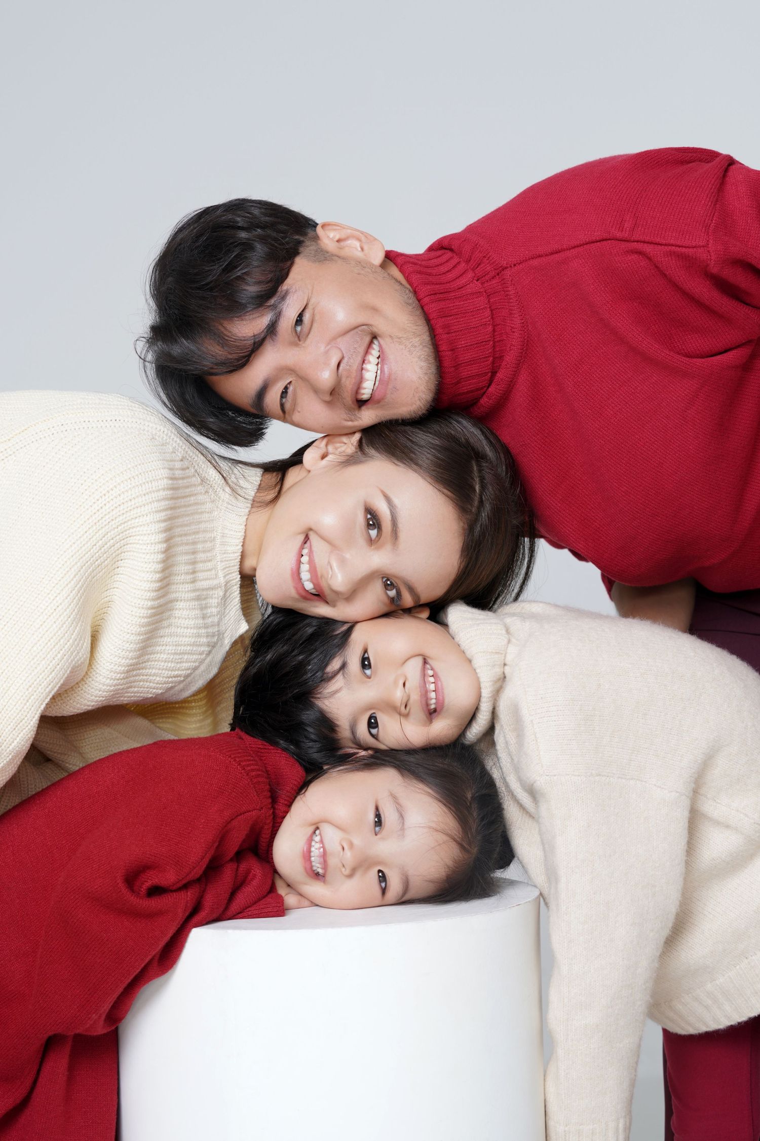 Four people wearing red and cream colored sweaters lean together while smiling against a white background.