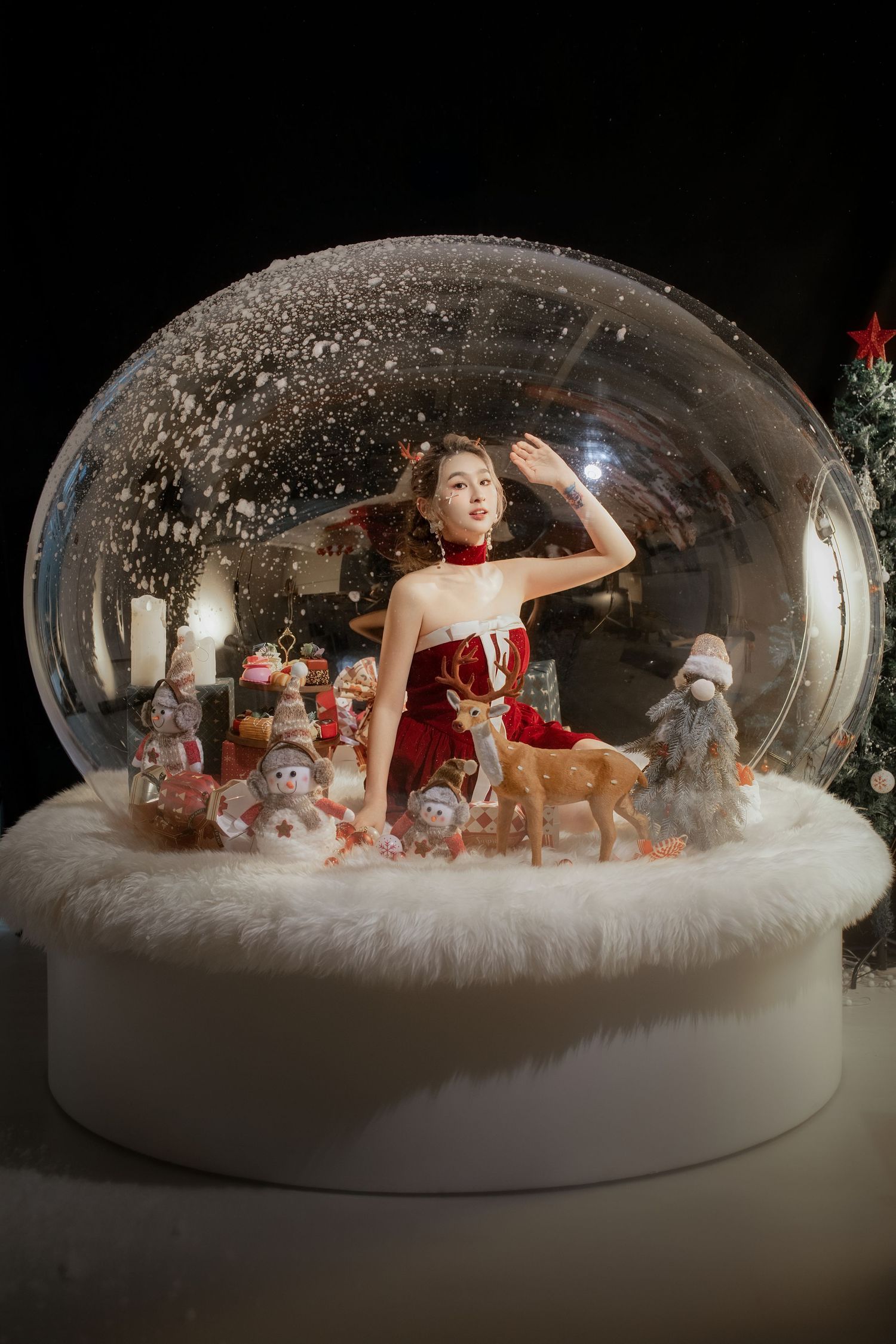 A festive snow globe scene with a figure in red dress surrounded by holiday decorations and winter characters.