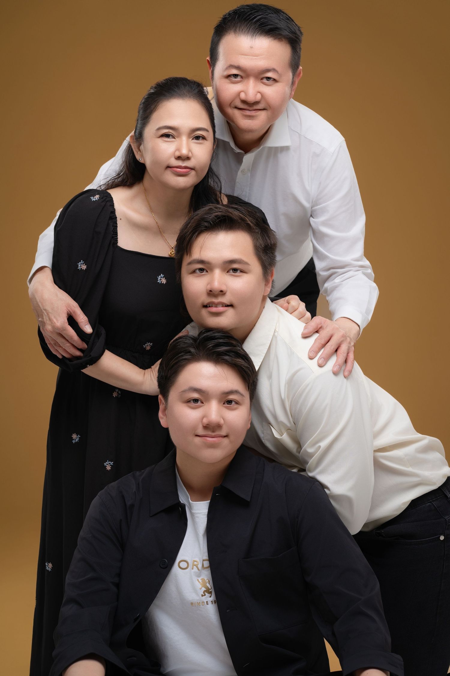 Asian family of four posing together in studio portrait against golden background, wearing black and white outfits.