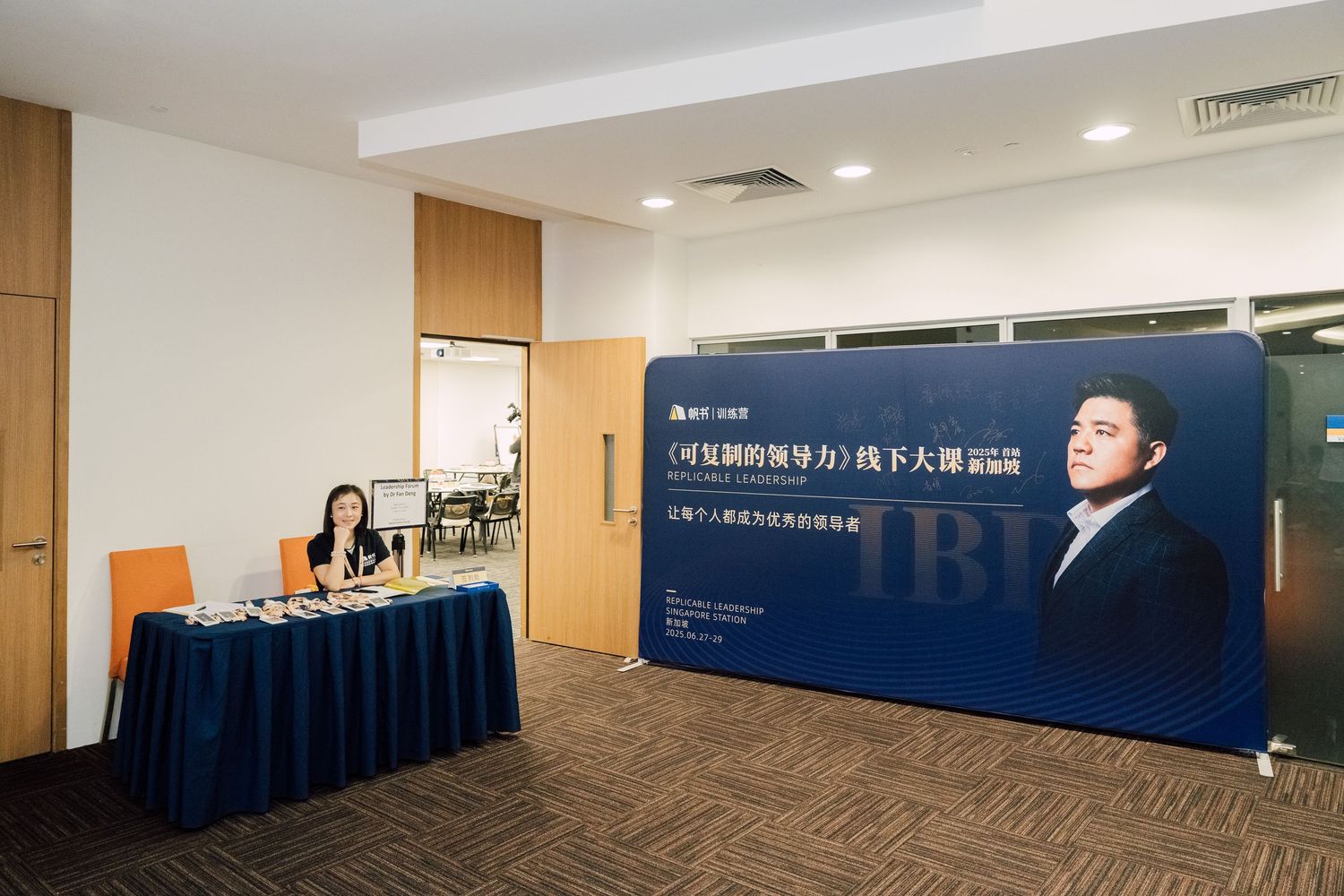 Professional seminar setup with Chinese banner, a woman at registration desk, and a speaker backdrop in a modern conference room.