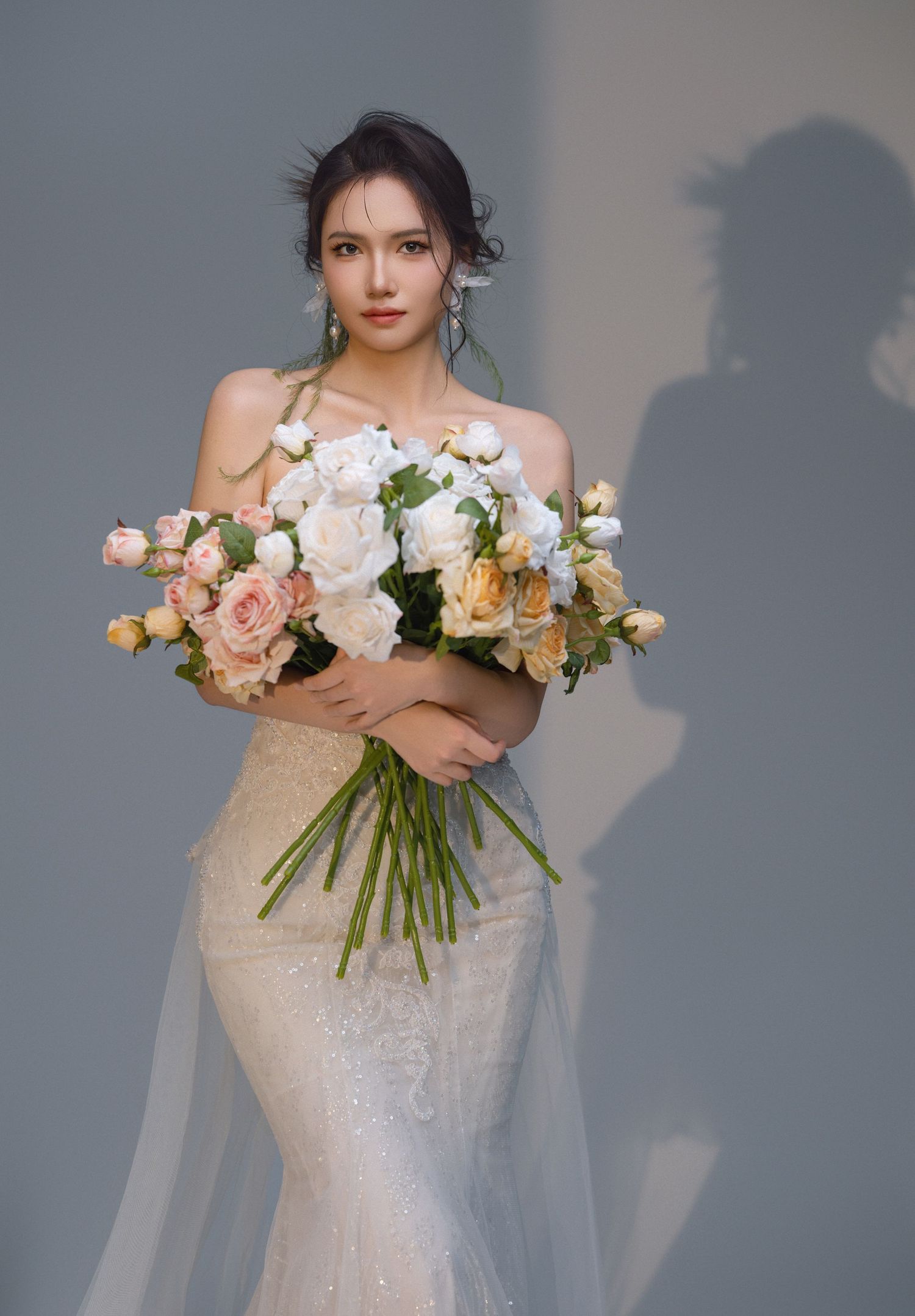Elegant bride in strapless mermaid gown holding large bouquet of white and peach roses for wedding photography.