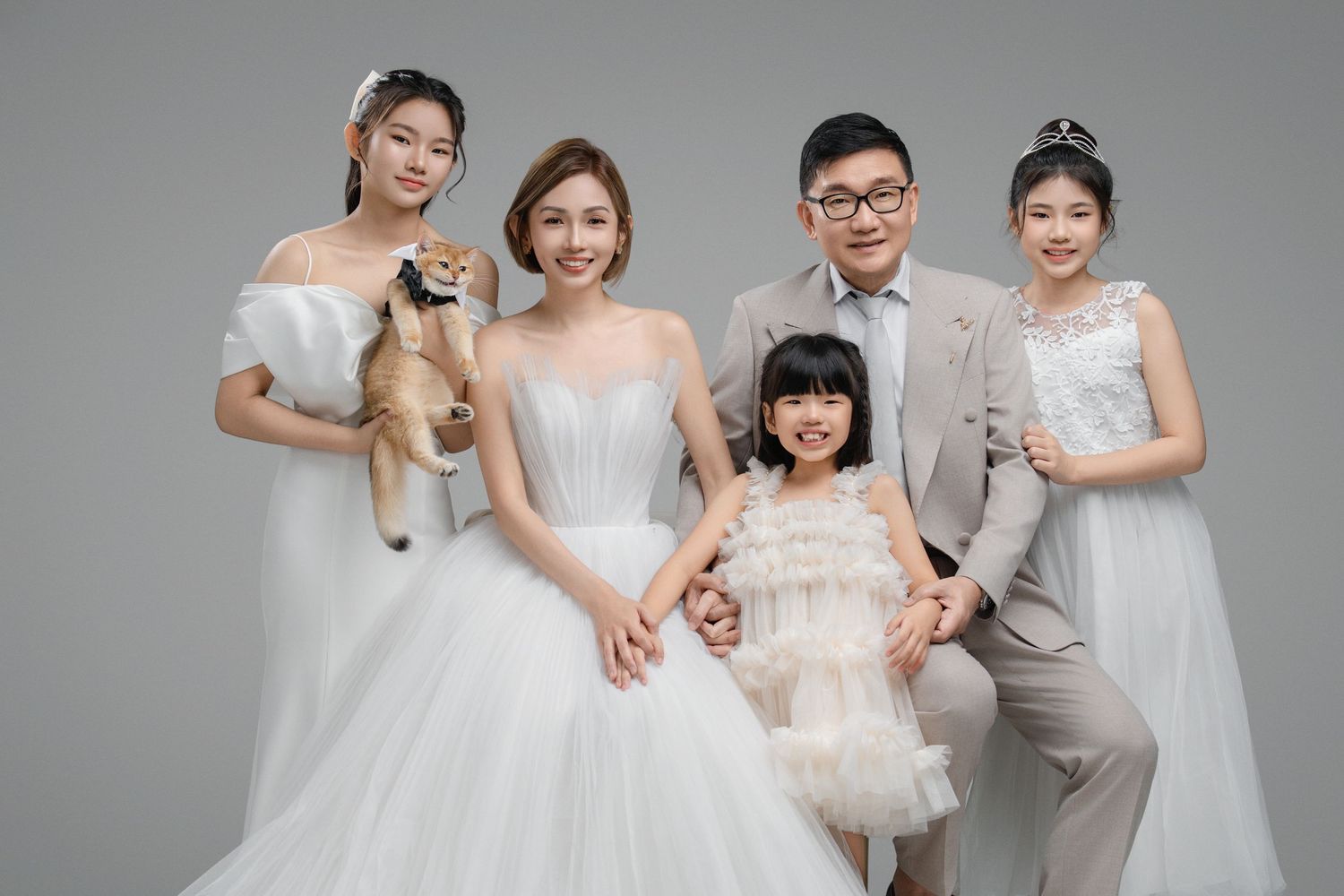 Family portrait in white formal wear with a small dog, posing together in a studio setting.