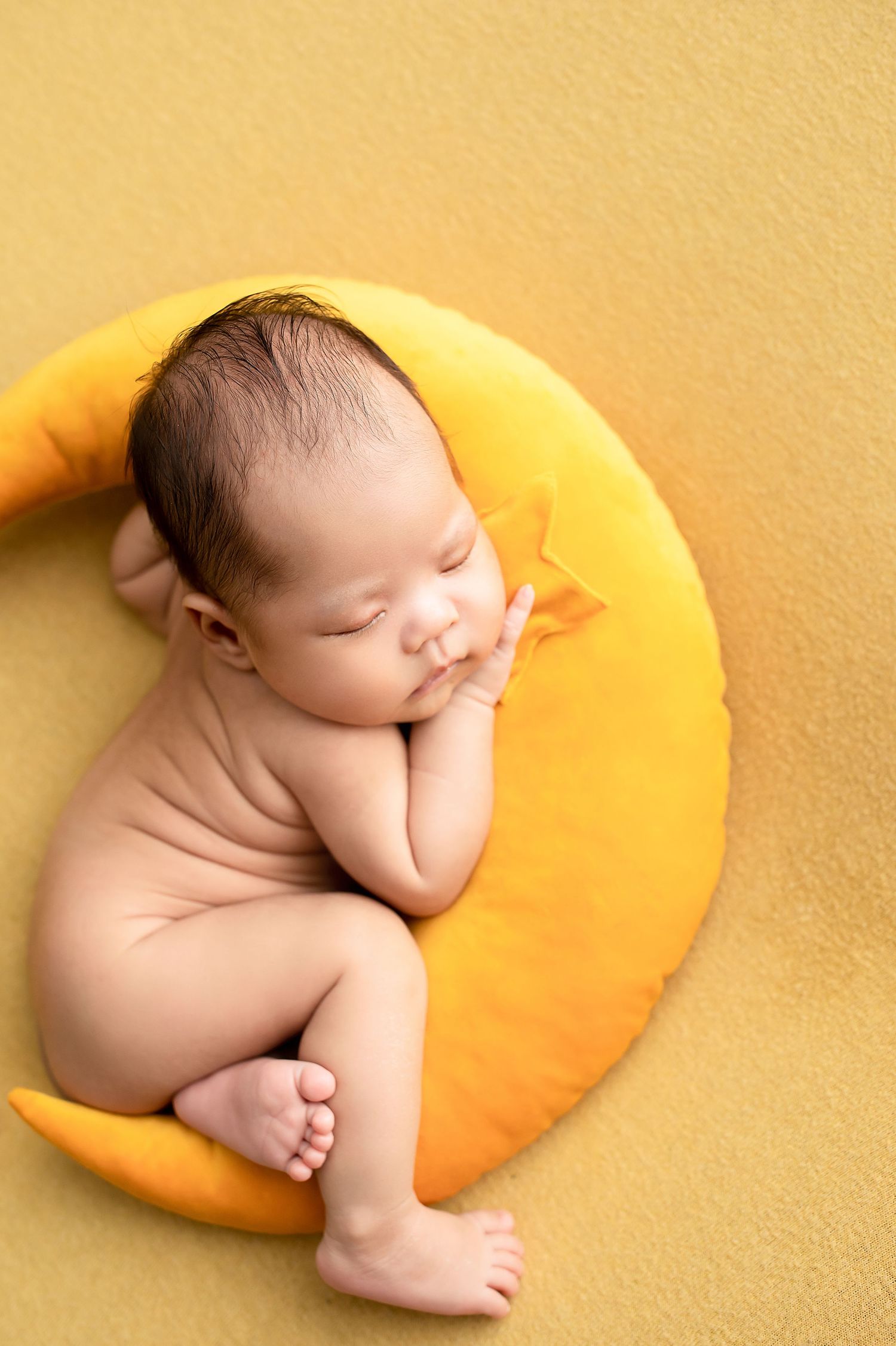 Sleeping newborn baby curled up on a soft yellow cushion in a peaceful pose.
