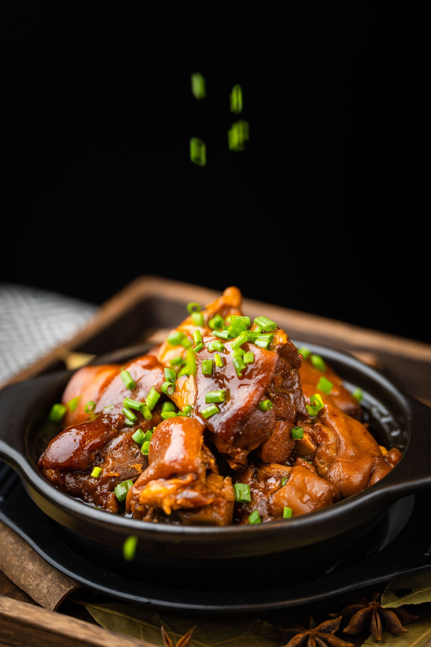 Braised pork knuckle in savory sauce topped with fresh green onions served in a black cast iron bowl.