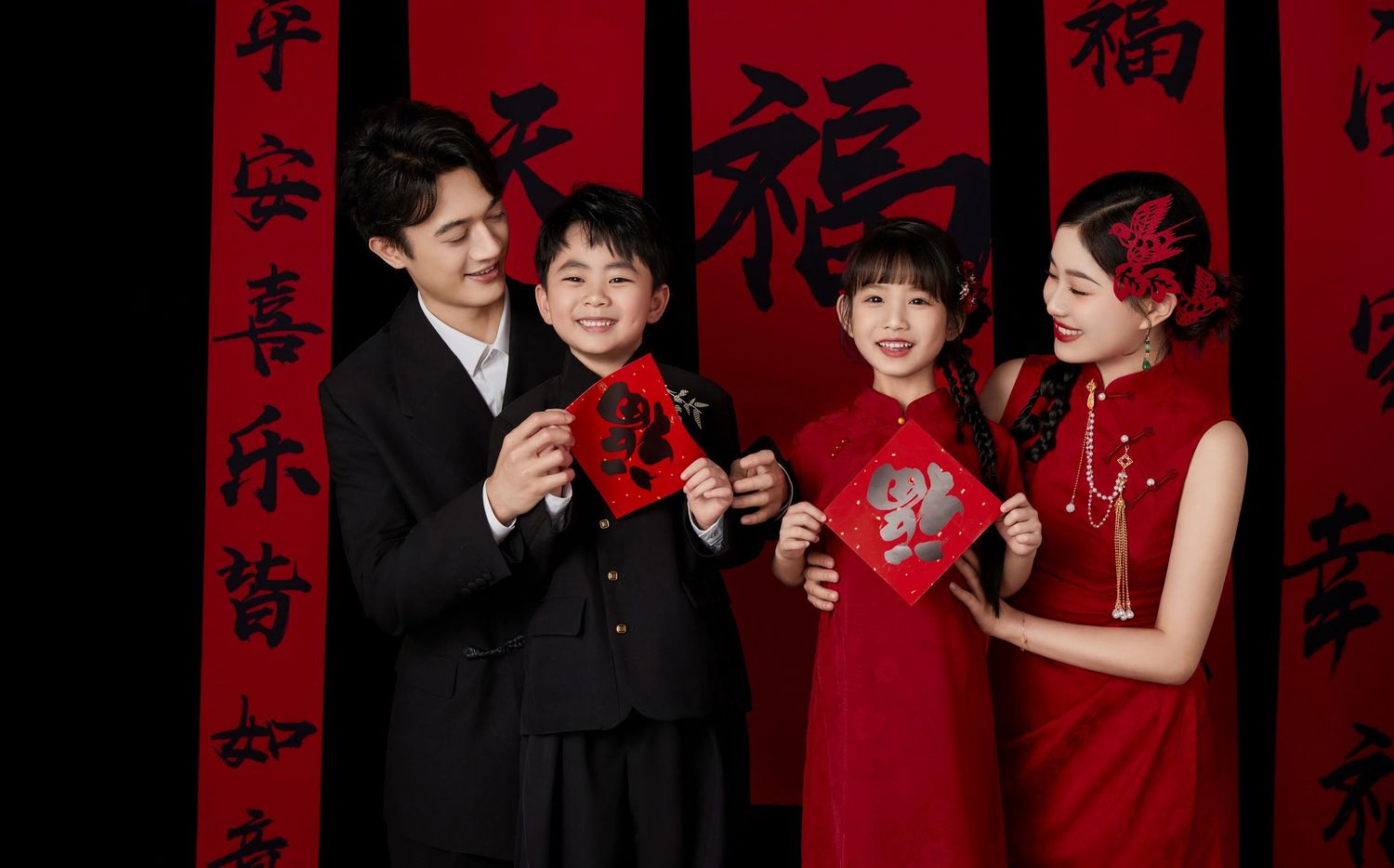 Chinese family of four in traditional red attire holding festive decorations against a backdrop of calligraphy banners.