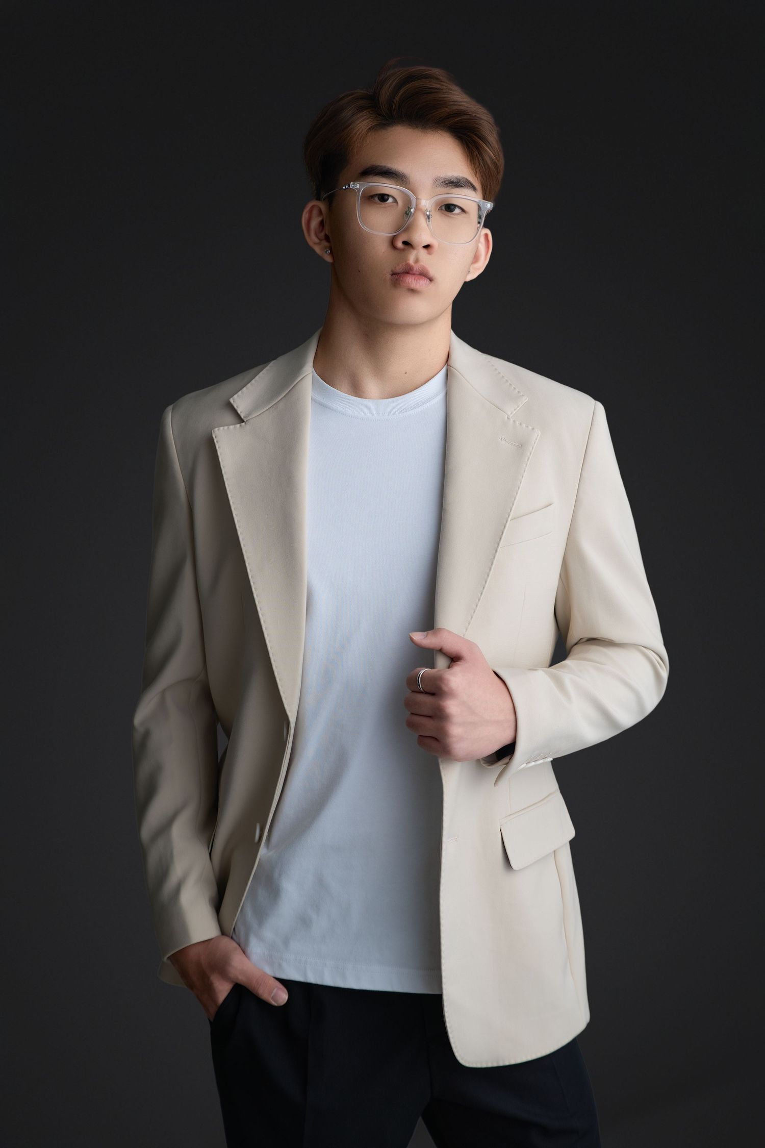 Professional studio portrait of a person wearing a cream blazer and white t-shirt against a dark background.