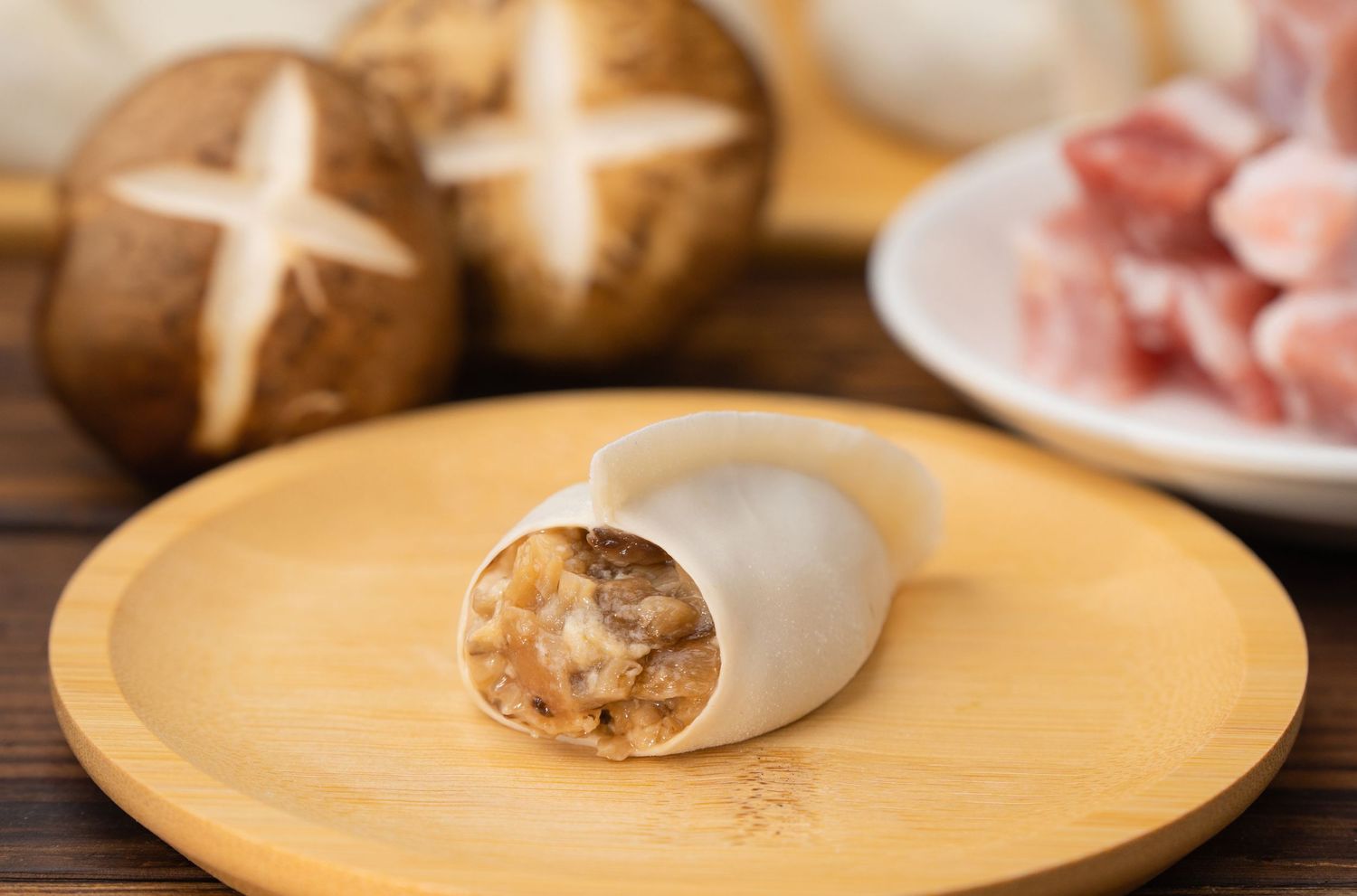 Sliced dumpling roll filled with mushroom and pork stuffing on wooden board with shiitake mushrooms in background.