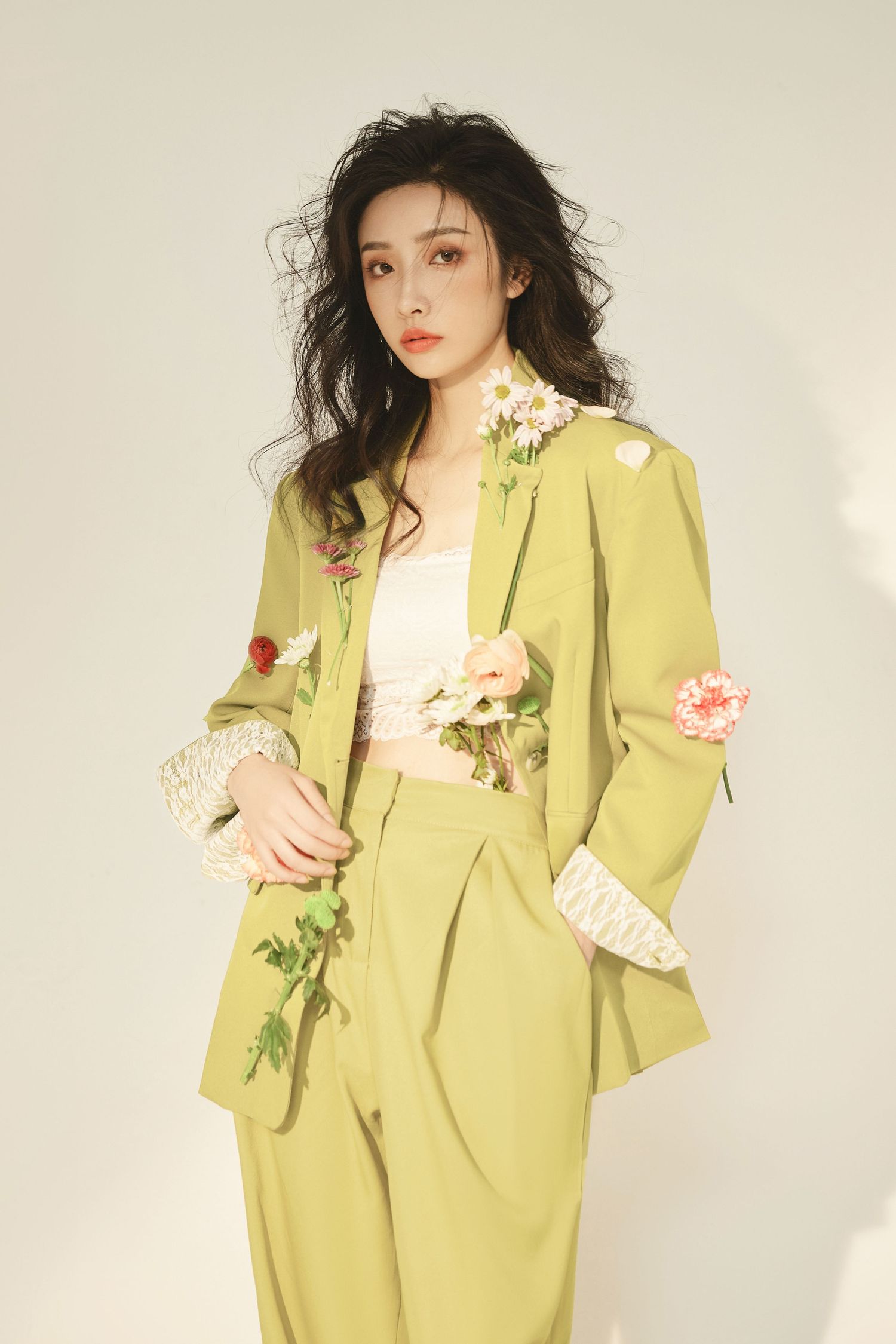 A person wearing a light green floral suit with pink roses and white ruffled sleeves poses against a neutral backdrop.