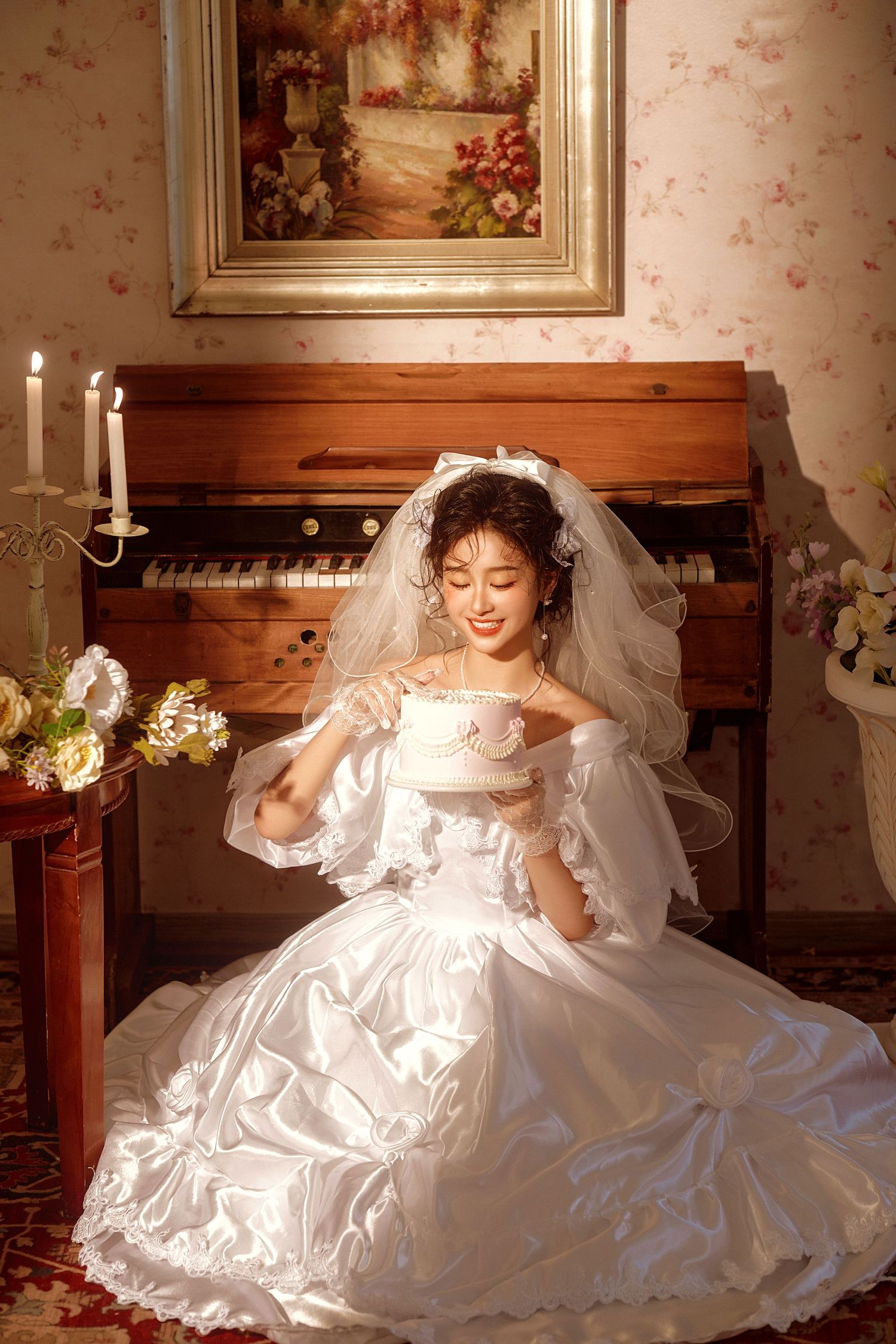 A bride in a flowing white wedding dress and veil poses elegantly in a vintage-style room with floral wallpaper and candlelight.