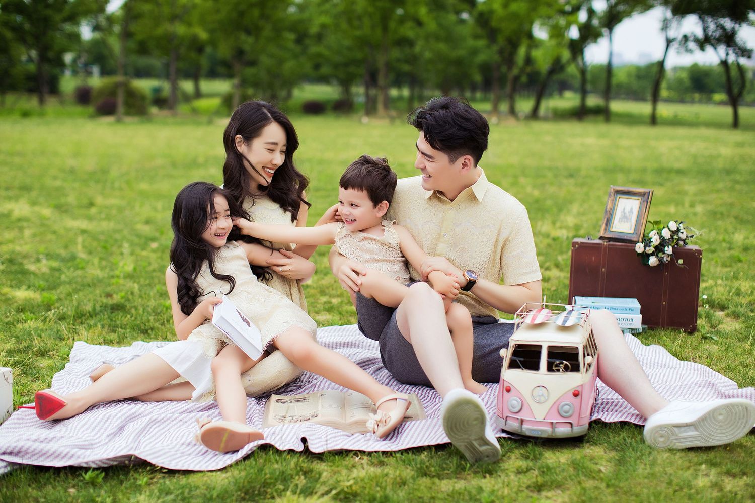 Family enjoying a relaxing summer picnic on a blanket in a green park with snacks and drinks.