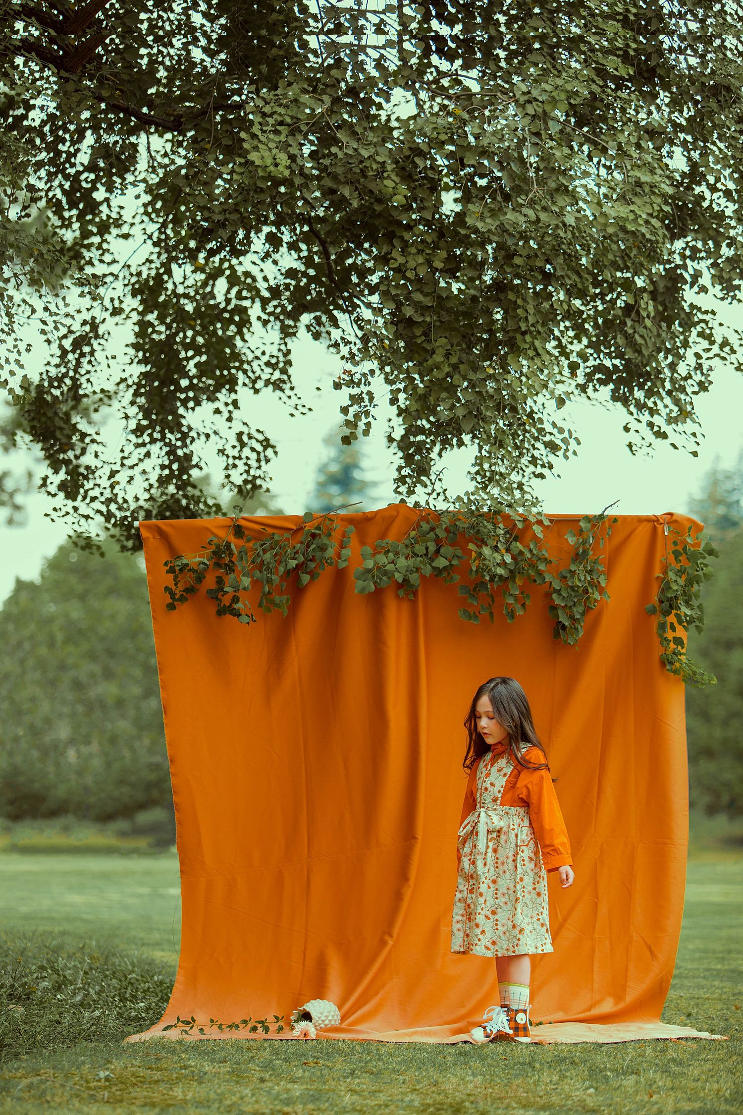 A creative photo series showing someone peeking out from behind an orange backdrop in an outdoor garden setting.