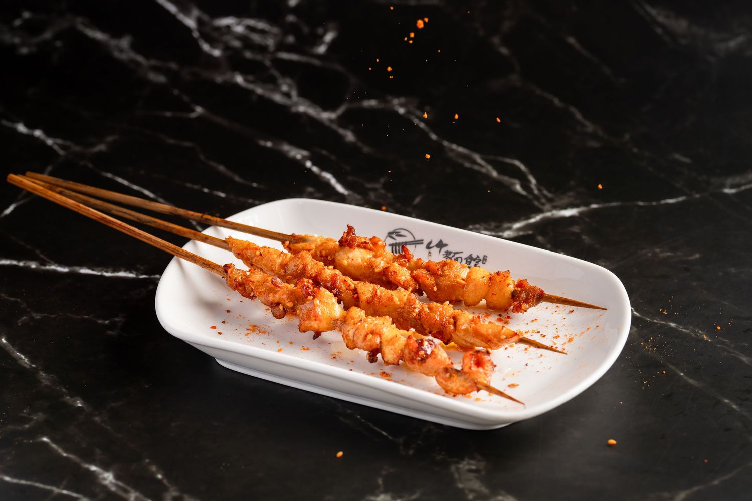 Spicy grilled shrimp skewers served on a white rectangular plate on a dark marble surface.