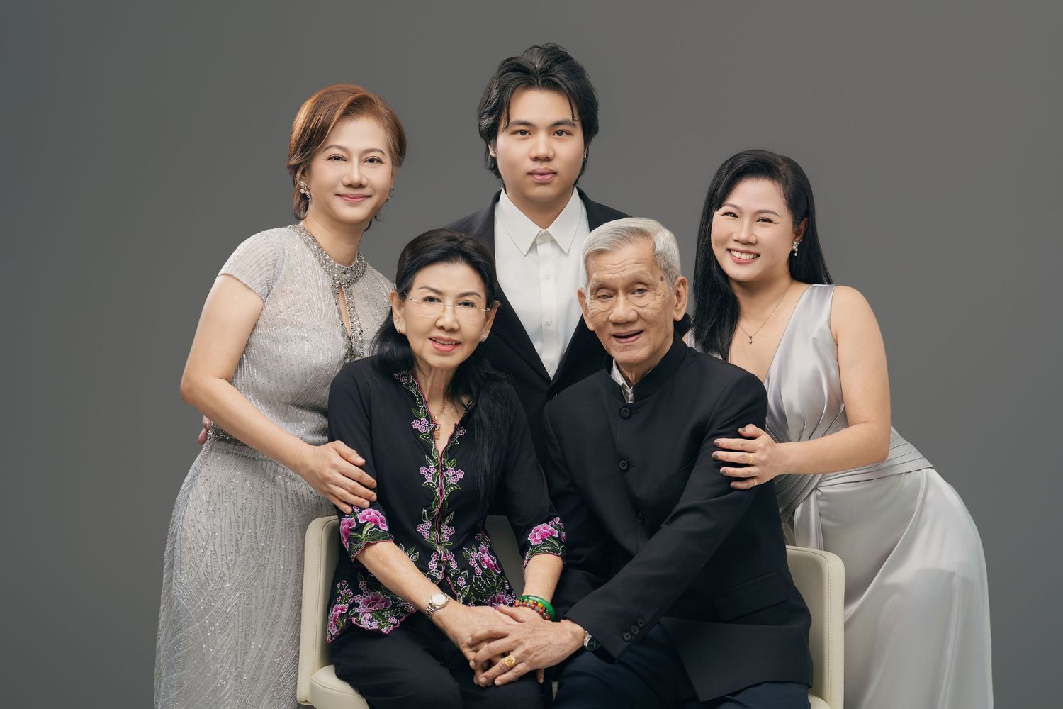 A formal family portrait of five people posing together against a gray background in elegant attire.