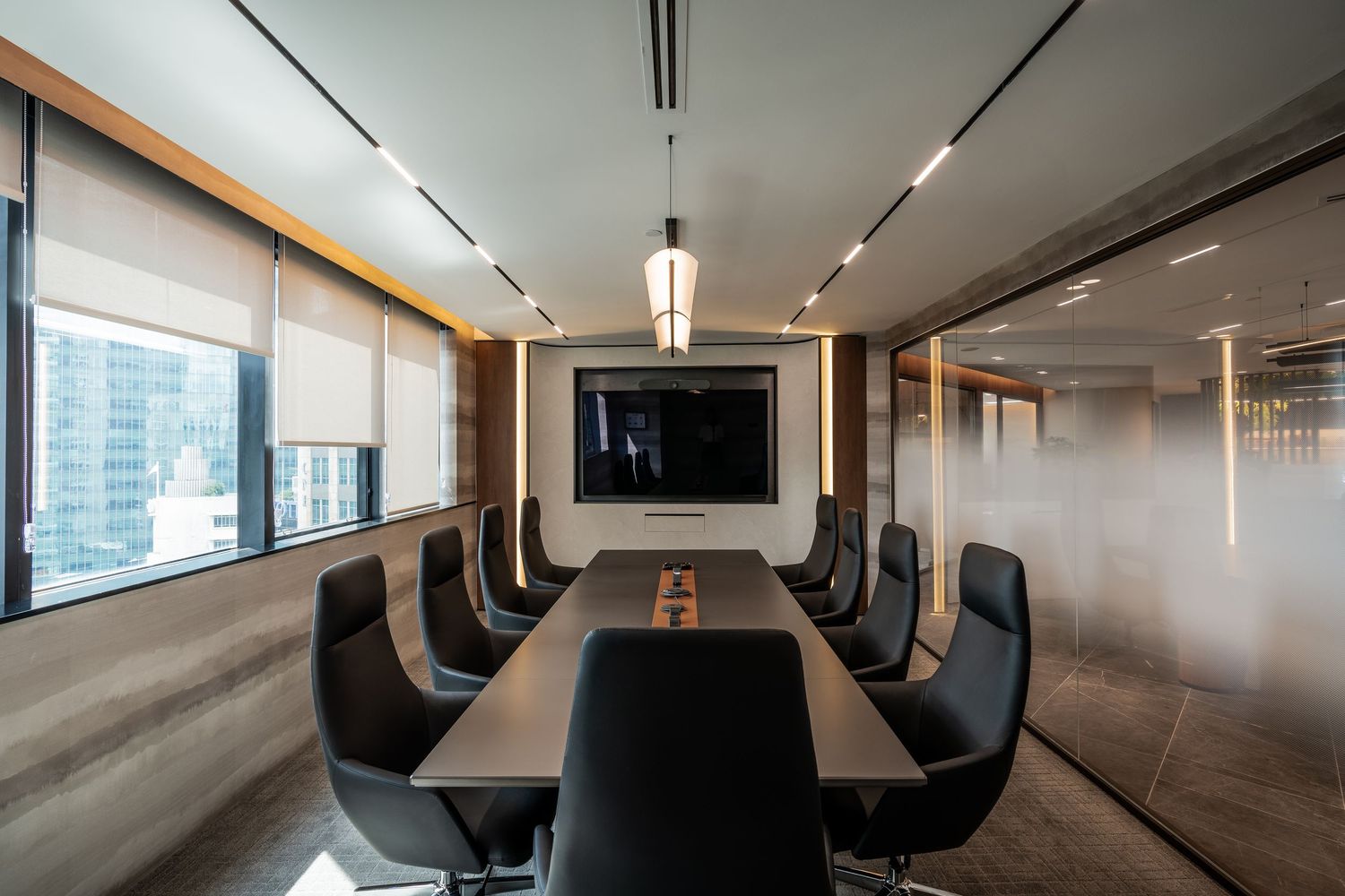 Modern corporate conference room with long black table, leather chairs, wall-mounted TV, and floor-to-ceiling windows.