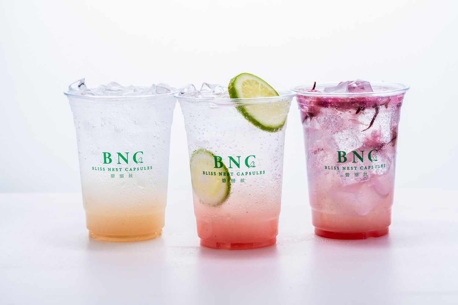Three BNC branded iced drinks in clear cups, featuring lime and cherry blossom garnishes on a white background.