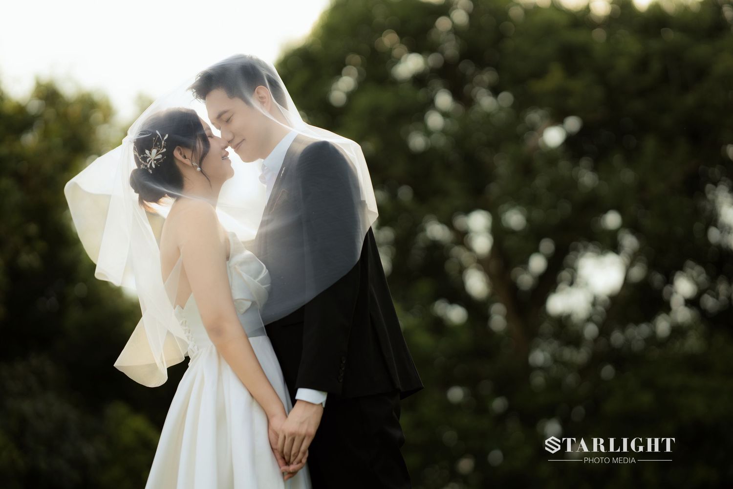 Romantic wedding couple sharing an intimate moment outdoors, bride in white gown with veil, groom in black suit.