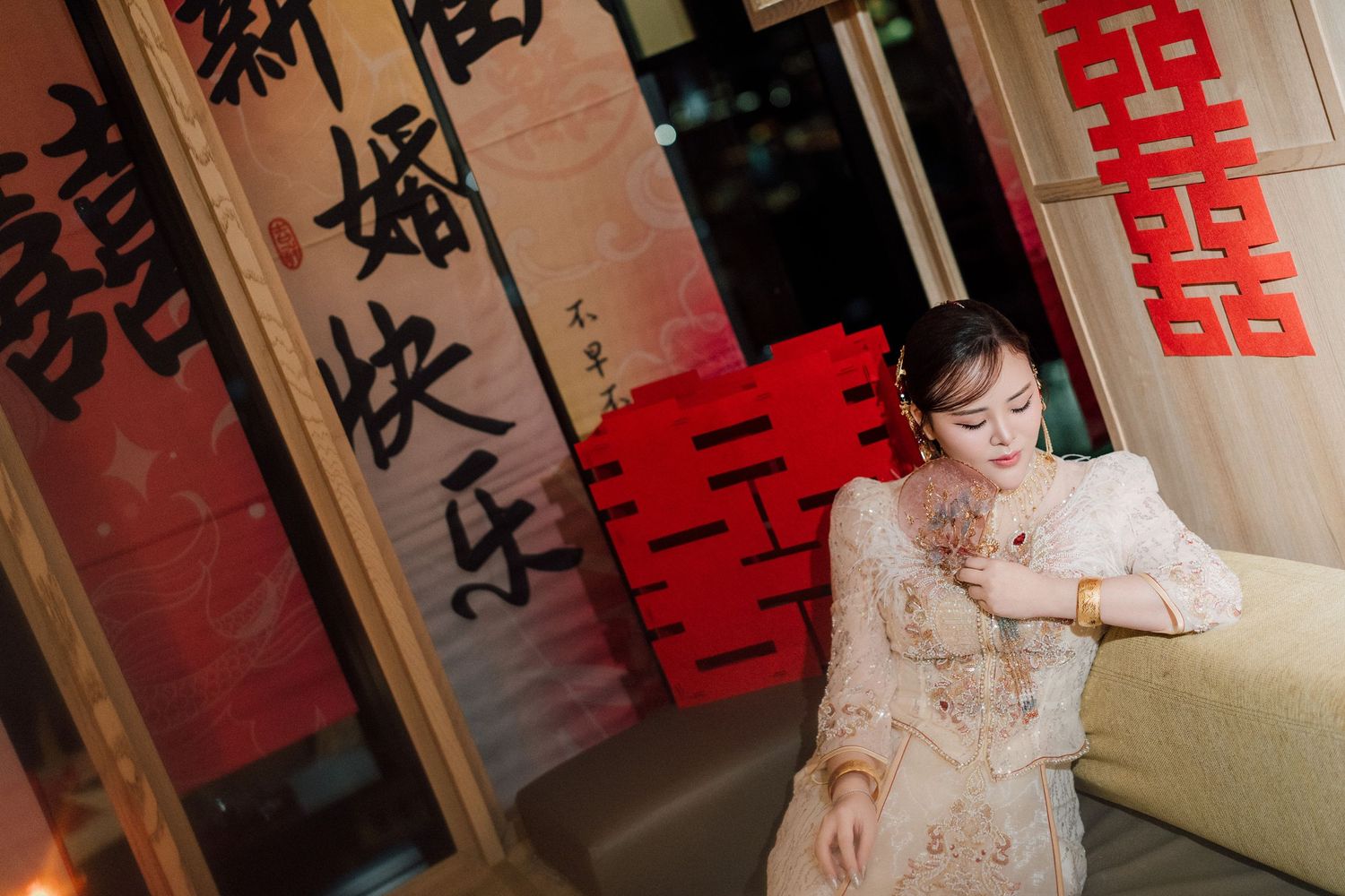 Traditional Chinese interior with red decorative banners and a qipao dress near a beige couch.