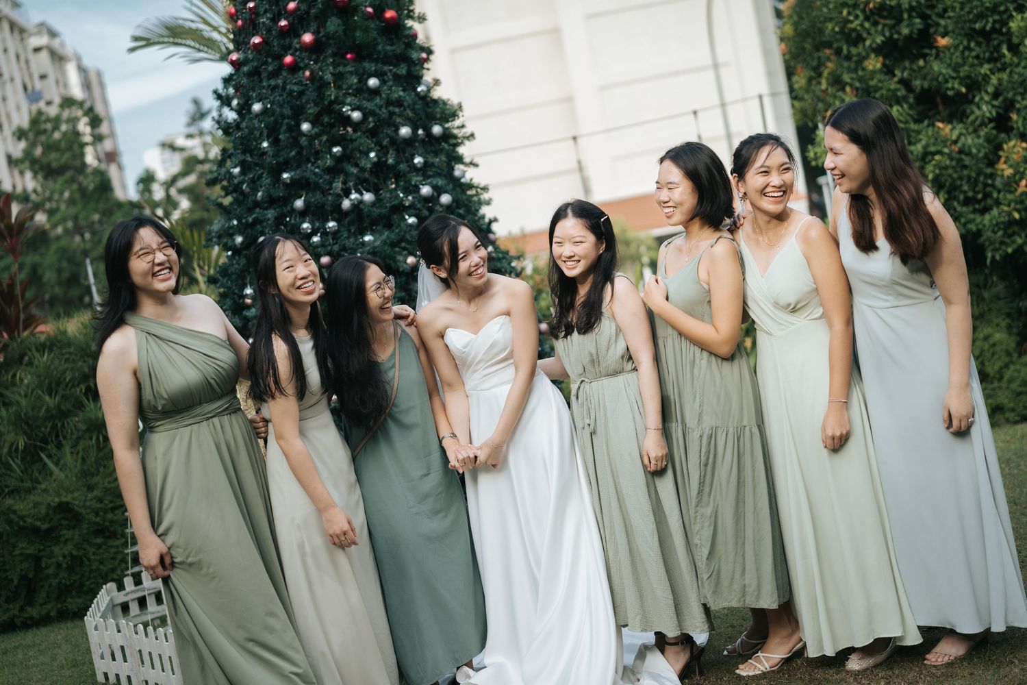 Wedding party in sage green and white dresses poses together in matching outfits for outdoor group photos.
