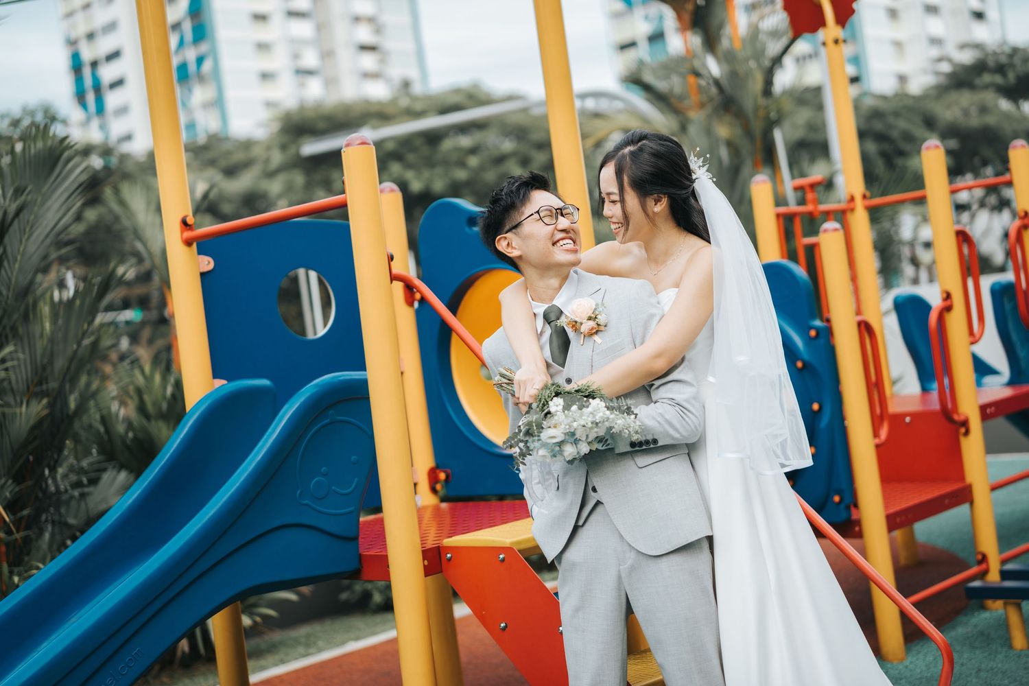 A couple shares a romantic moment at a colorful playground with slides and climbing equipment on a sunny day.