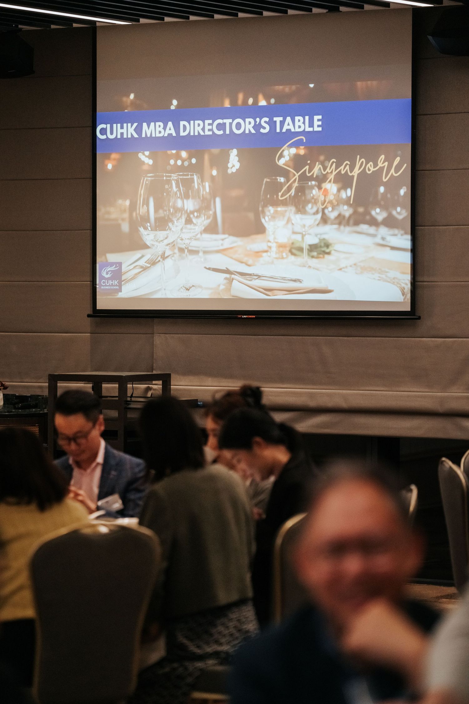 CUHK MBA Director's Table Singapore event with attendees dining in a conference room with a projected presentation screen.