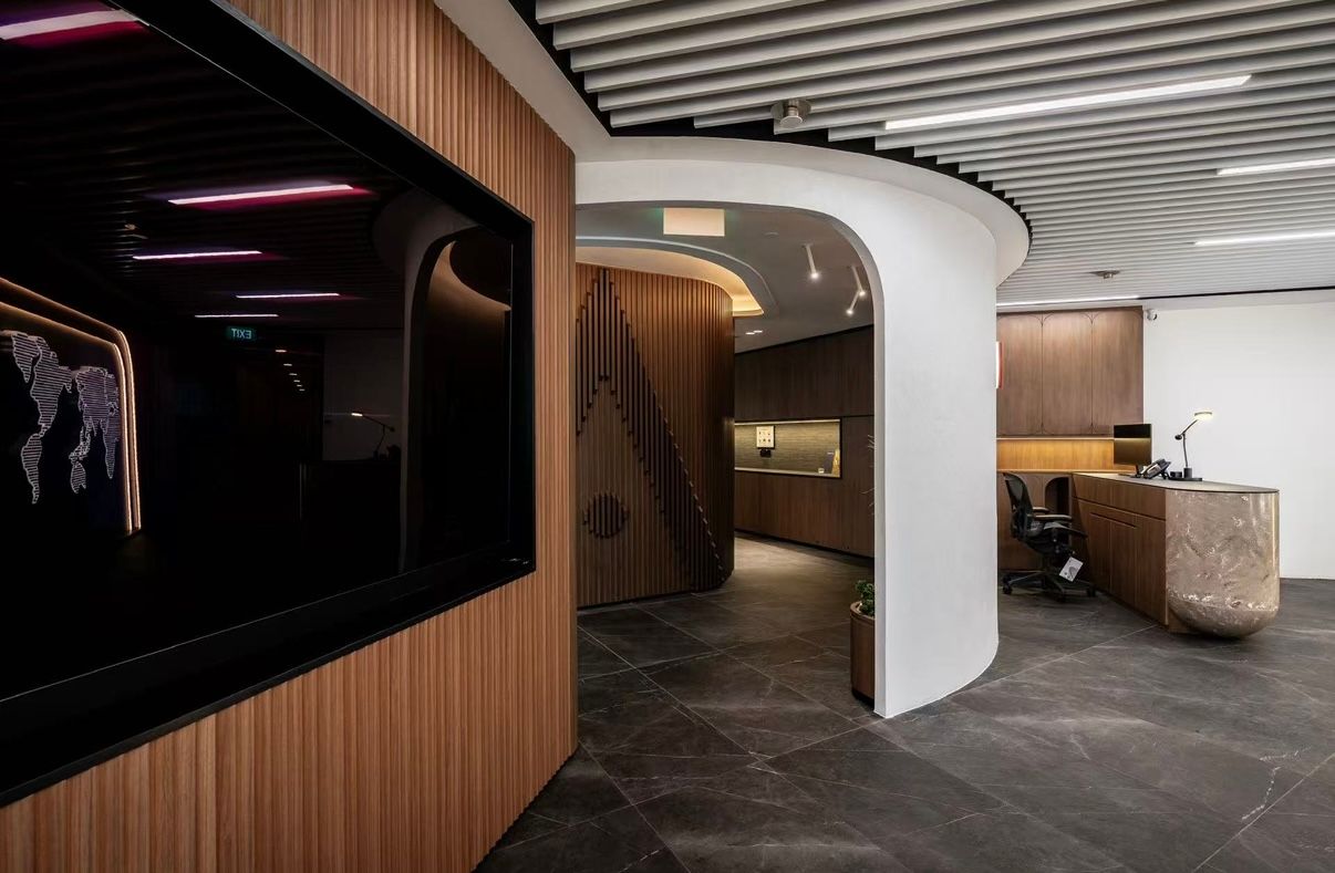 Modern office interior featuring curved white walls, wood paneling, dark stone floors, and a reception desk with warm lighting.