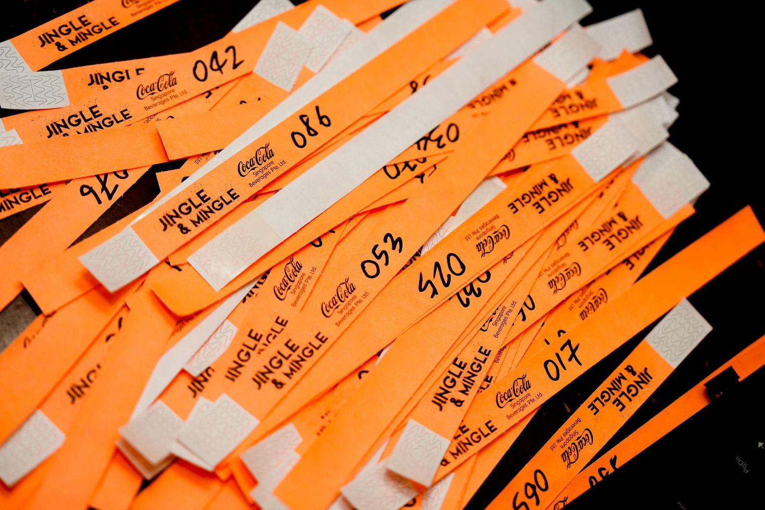 Orange wristbands with black numbers and Jingle Mingle Coca-Cola branding stacked together at an event.