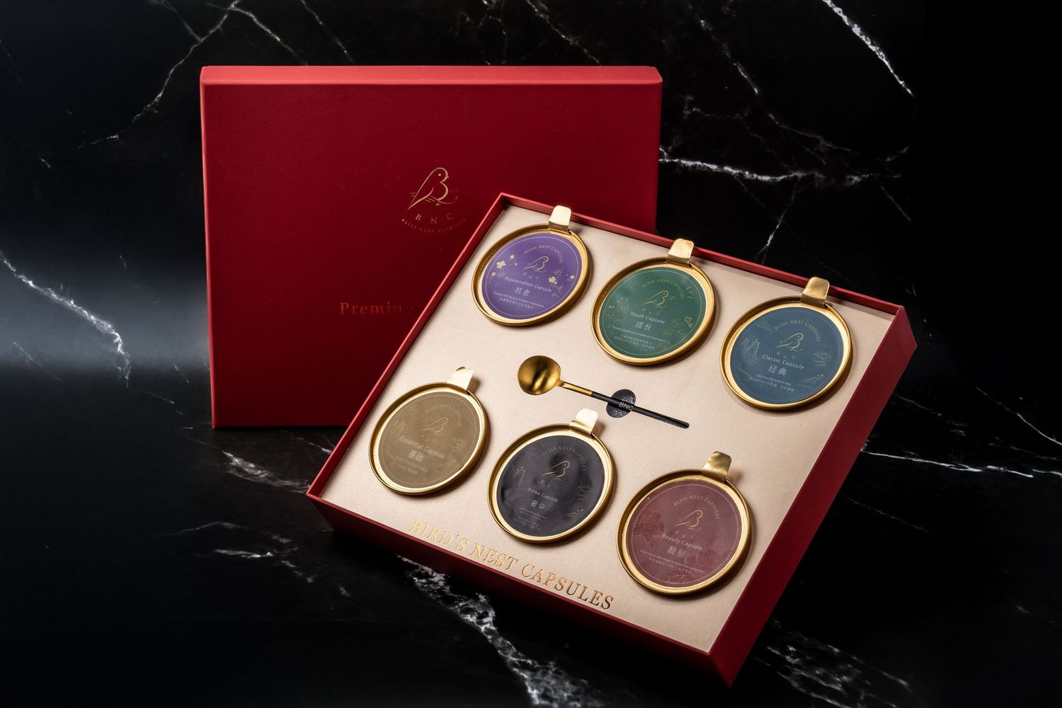 Luxury red gift box set with six colorful gemstone medallions in gold frames on cream velvet lining.