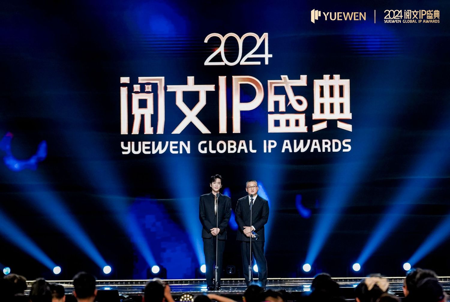 Two presenters on stage at the 2024 Yuewen Global IP Awards ceremony with illuminated Chinese signage backdrop.