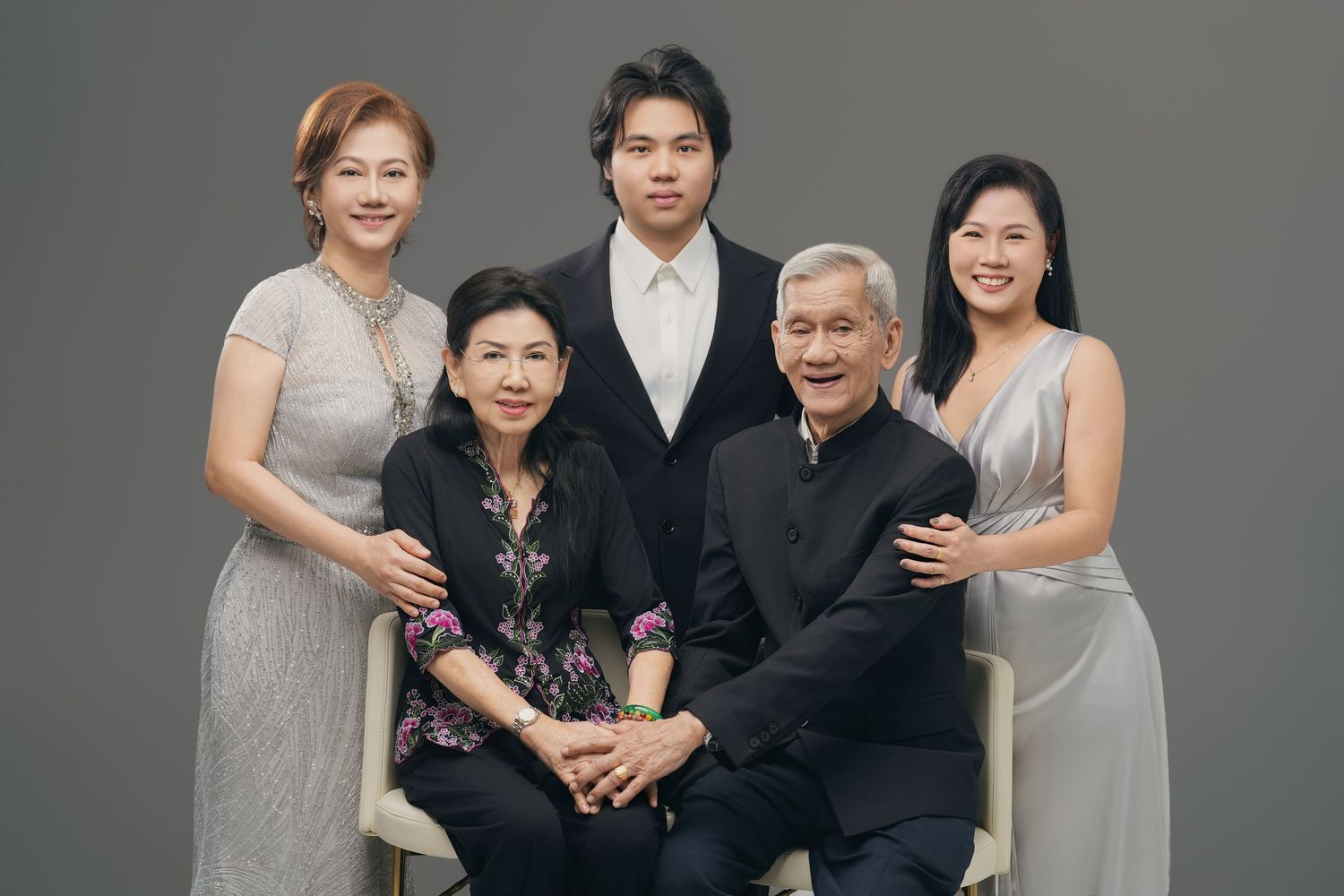 A joyful Asian family of five posing together for a formal portrait against a gray studio background.