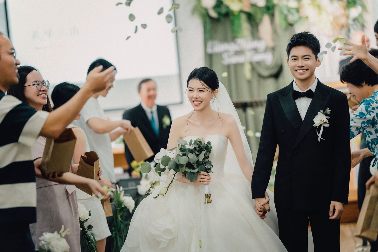 Smiling newlywed couple walks down the aisle as guests celebrate at an elegant indoor wedding ceremony.