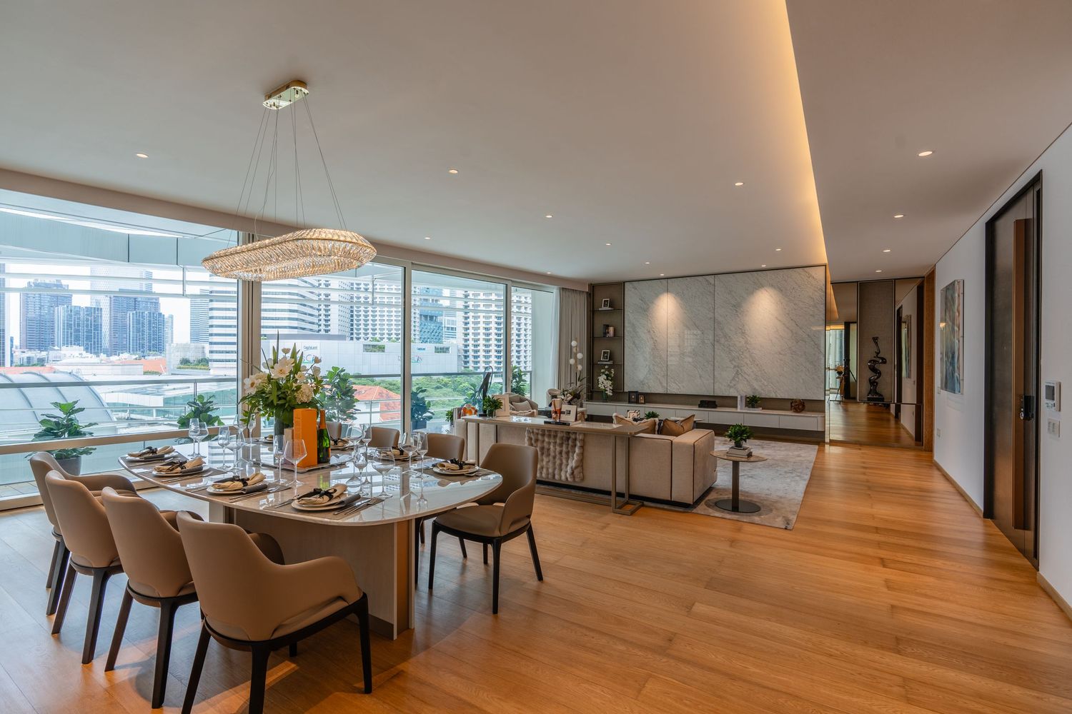 Modern open-plan dining and living room with hardwood floors, floor-to-ceiling windows, and elegant chandelier lighting.