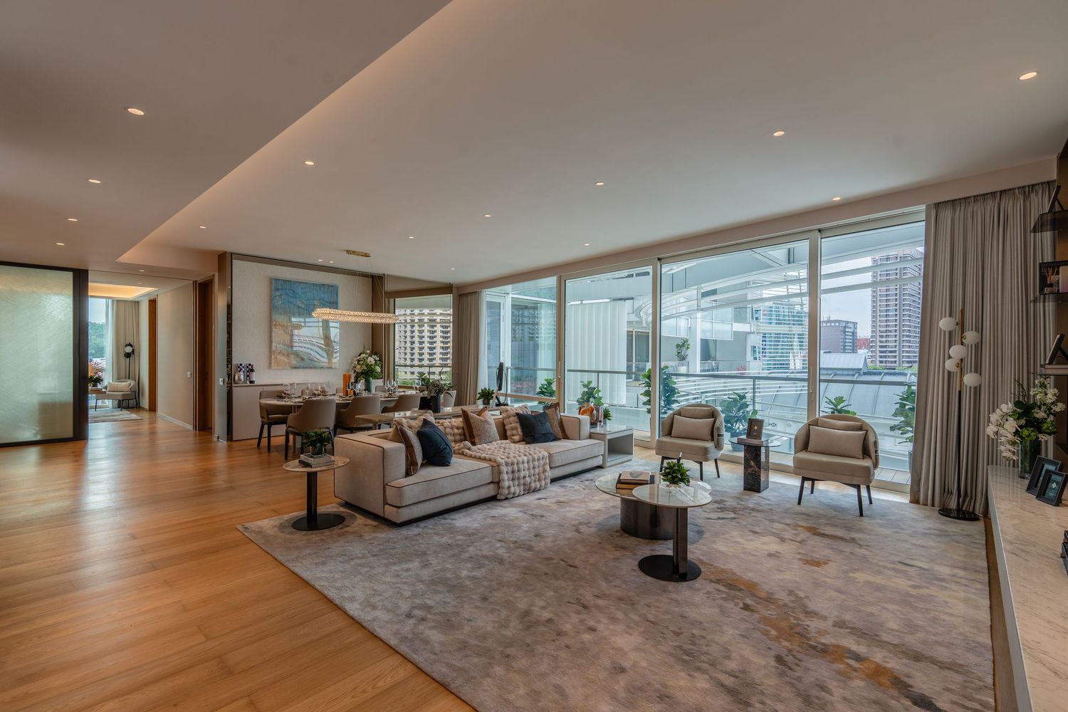 Spacious luxury living room with floor-to-ceiling windows, hardwood floors, neutral sofas, and city views.