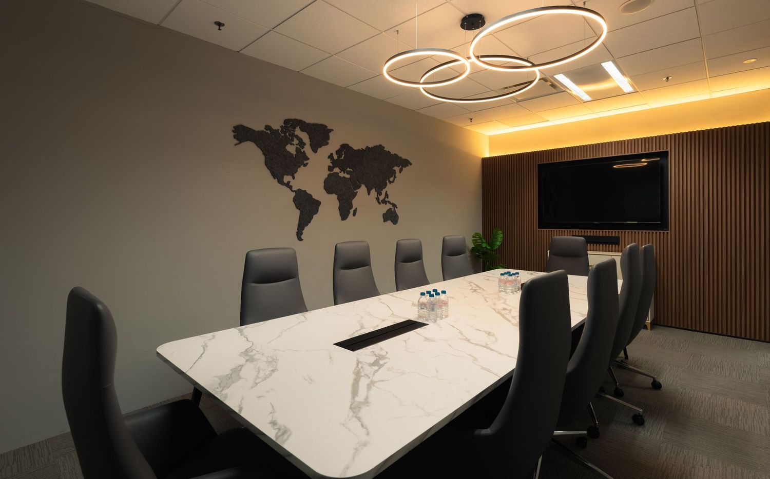 Modern conference room with marble table, black chairs, world map wall art, and circular LED light fixture.