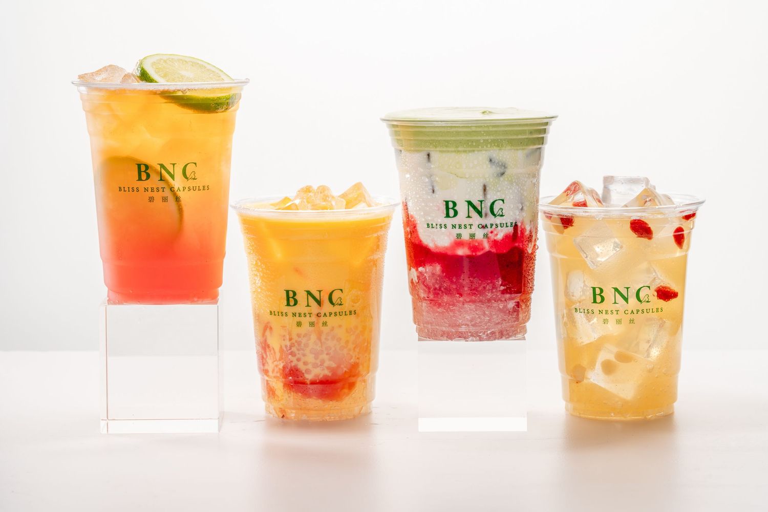 Four colorful BNC branded fruit drinks with ice displayed on clear acrylic stands against a white background.