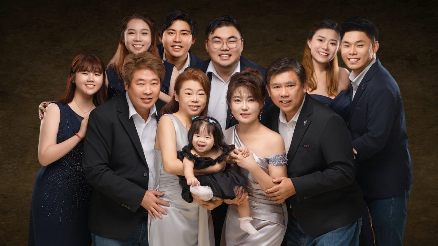 Large Asian family posing together in a professional studio portrait with elegant dark background.