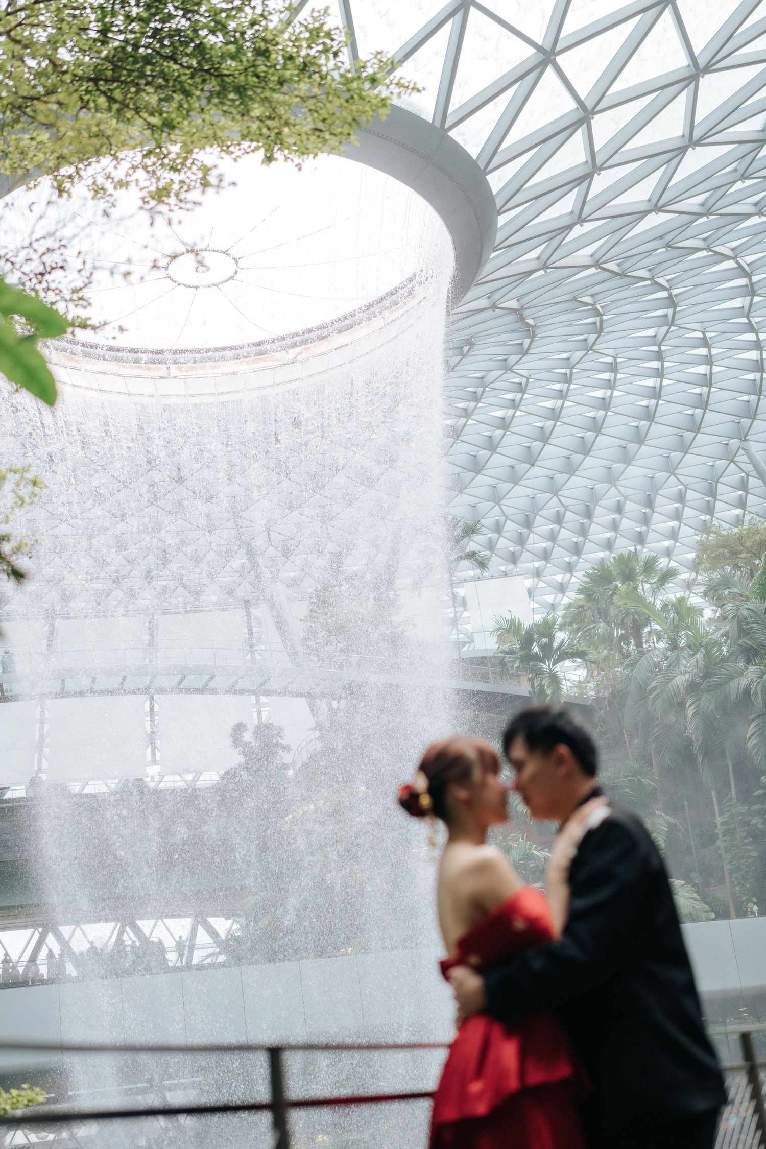Couple in wedding attire sharing a romantic moment in front of the stunning HSBC Rain Vortex at Jewel Changi Airport.