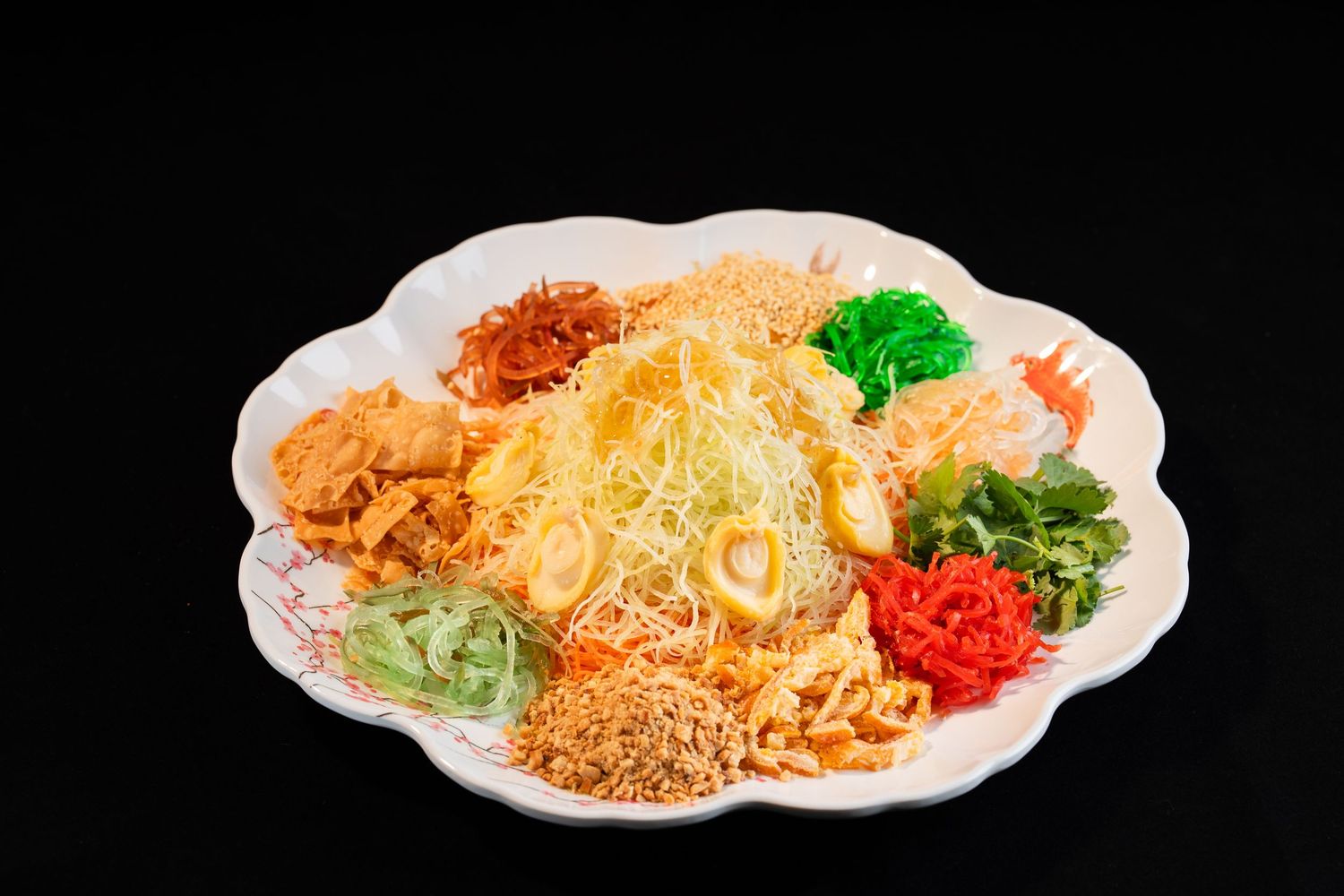 Colorful yusheng lo hei salad platter with shredded vegetables, noodles, and toppings on white plate.