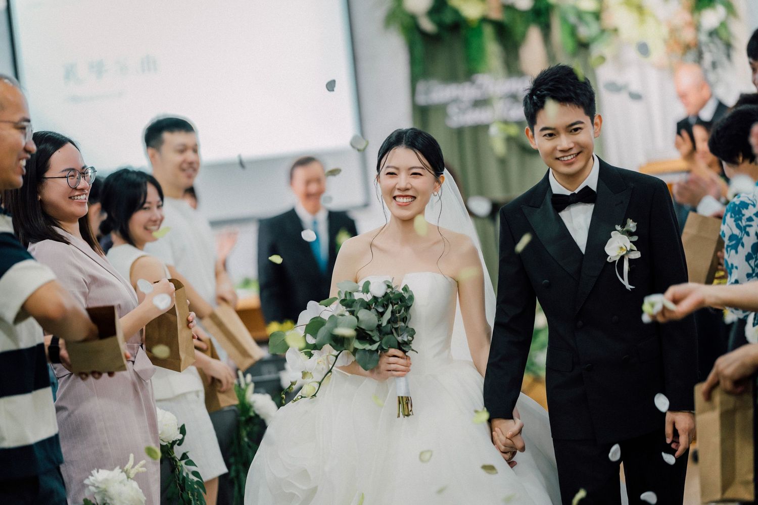 Wedding party celebrates joyfully during outdoor reception with natural greenery and formal attire.
